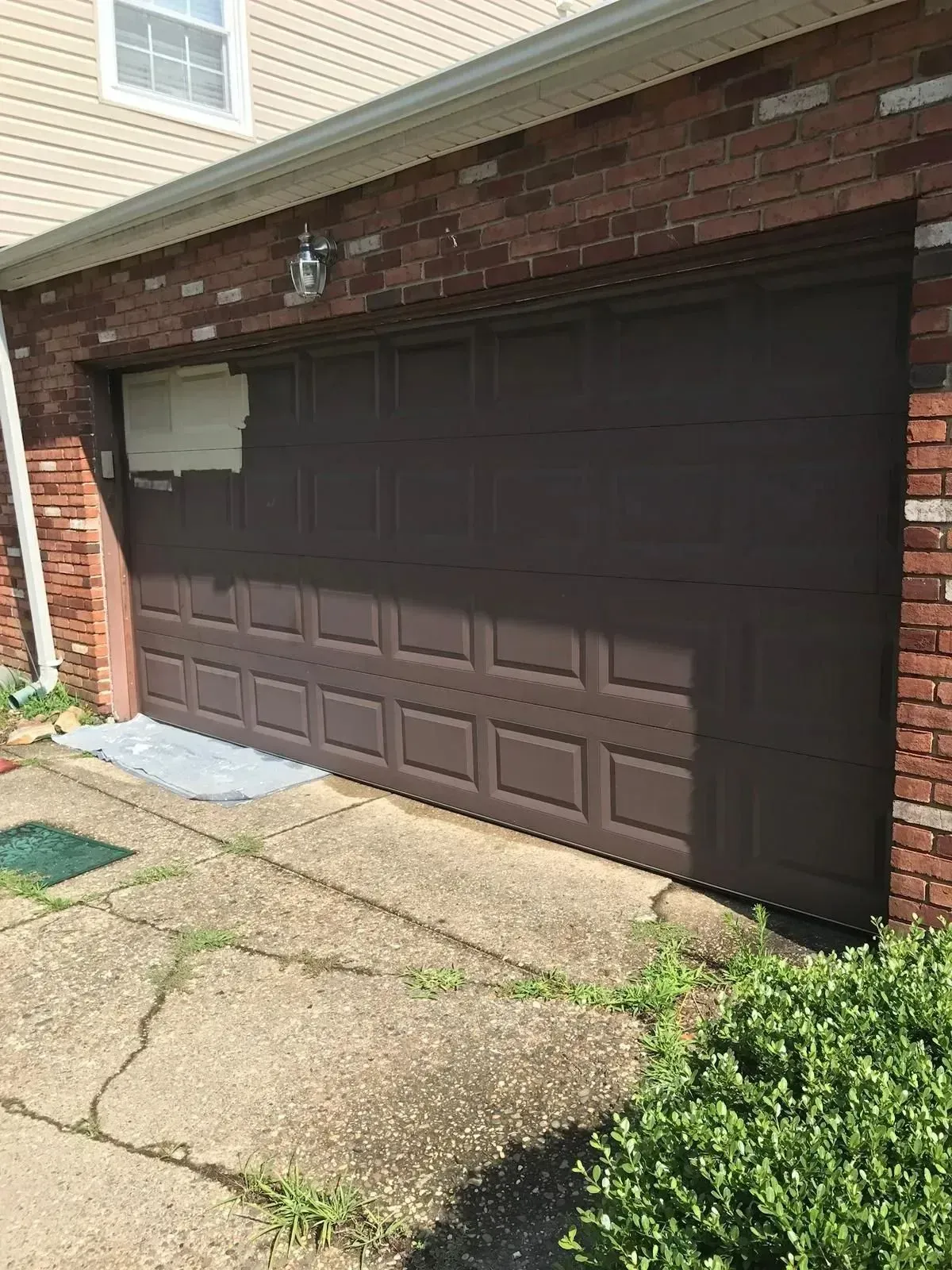 Brown garage door with brick exterior on a cracked concrete driveway.