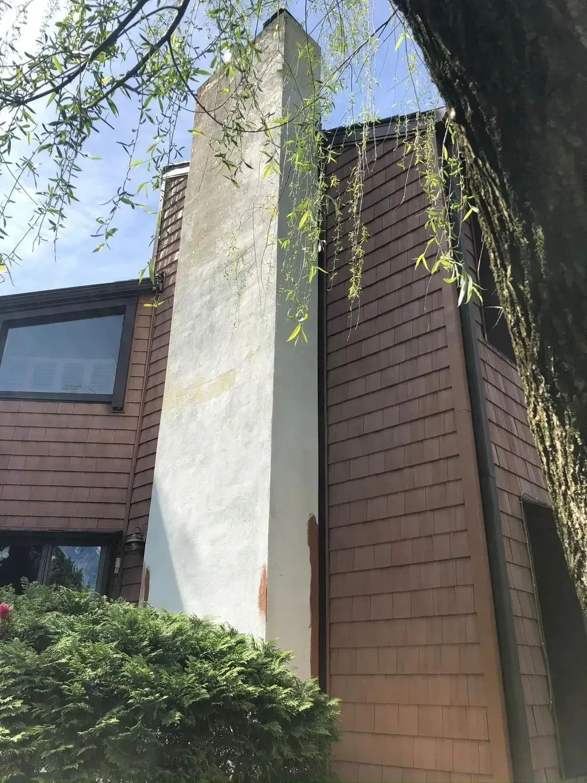 Tall, light-colored chimney attached to a brown shingled house.