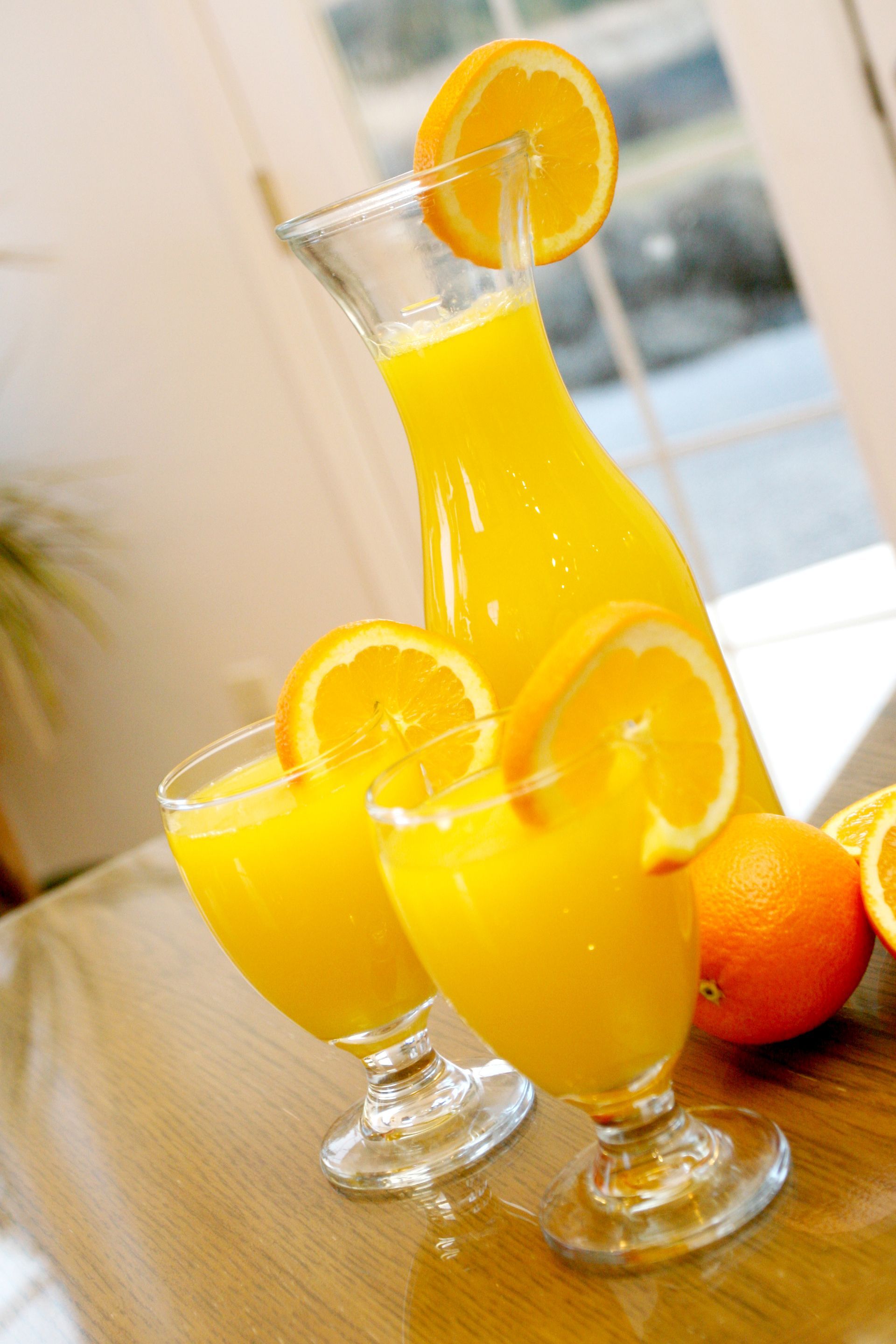 Carafe and glasses of orange juice with orange slice garnish on table.