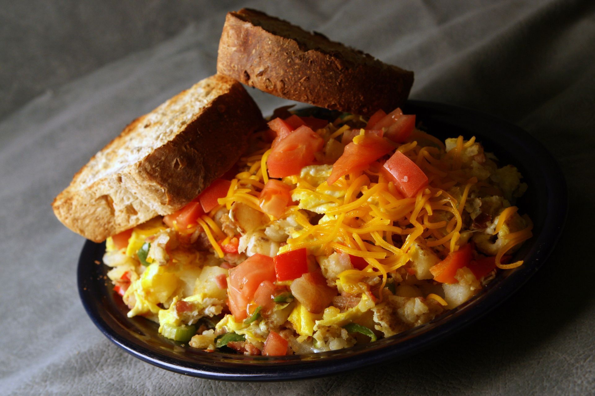 Scrambled eggs, potatoes, tomatoes, and cheese on a plate, with two pieces of toasted bread.