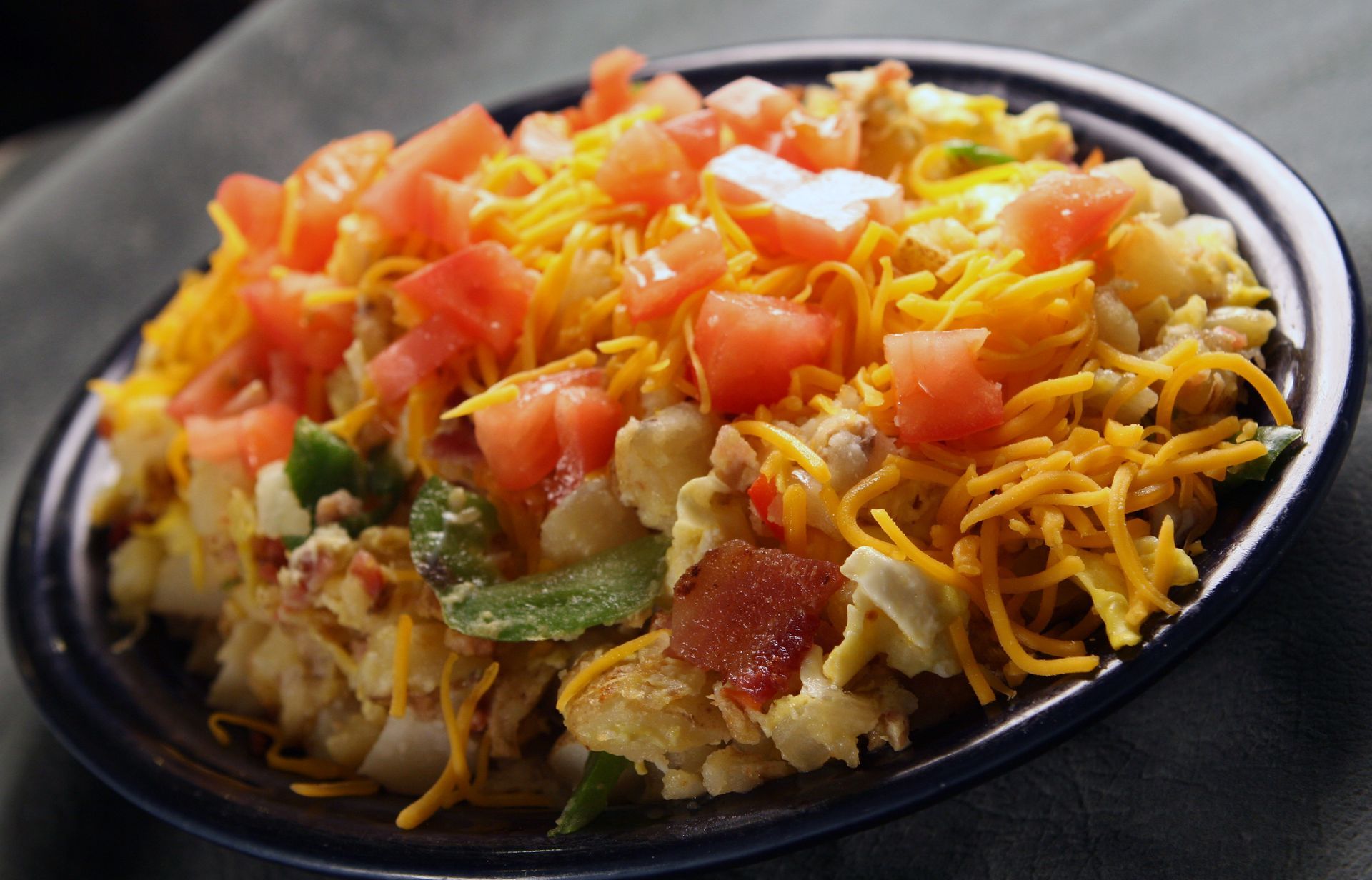 Scrambled egg breakfast dish with cheese, tomatoes, and bacon on a blue plate.