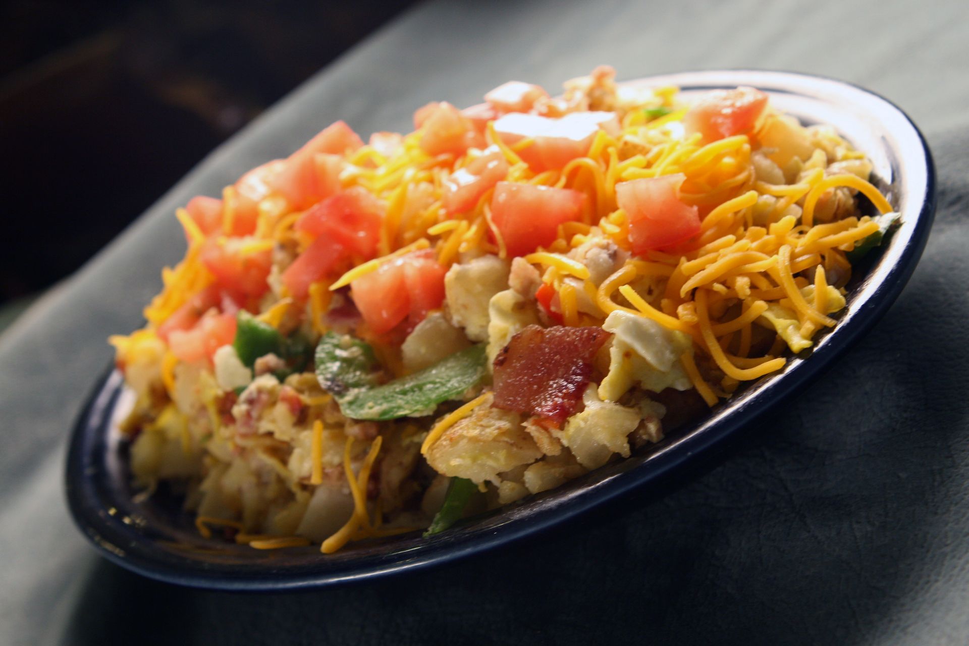 Scrambled eggs with bacon, diced tomatoes, cheese, and green peppers on a blue plate.