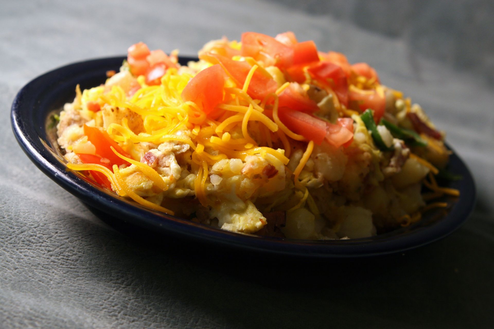 Potato hash topped with shredded cheddar cheese and diced tomatoes in a blue bowl.