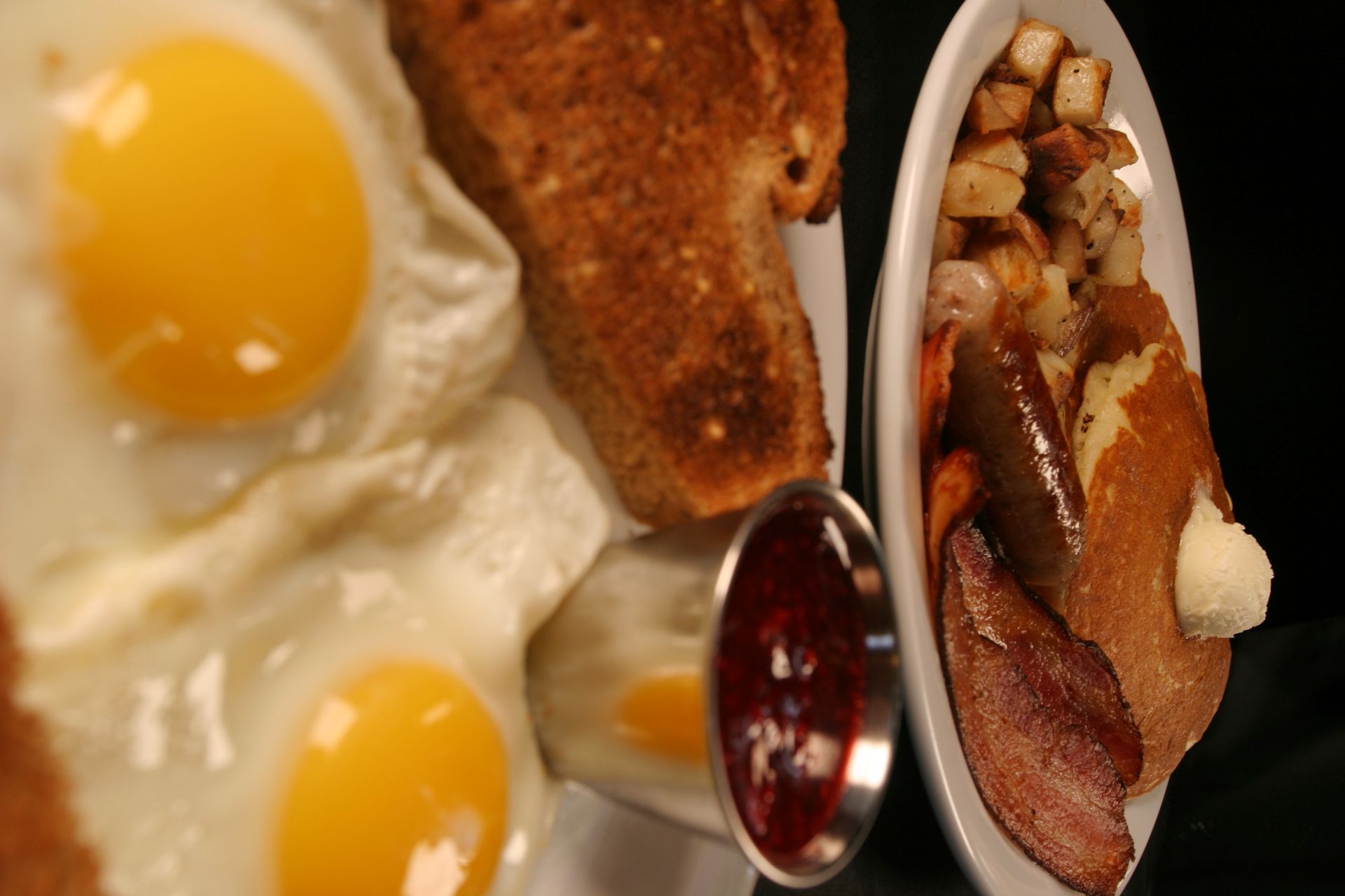 Breakfast plate with fried eggs, toast, potatoes, bacon, and jelly.