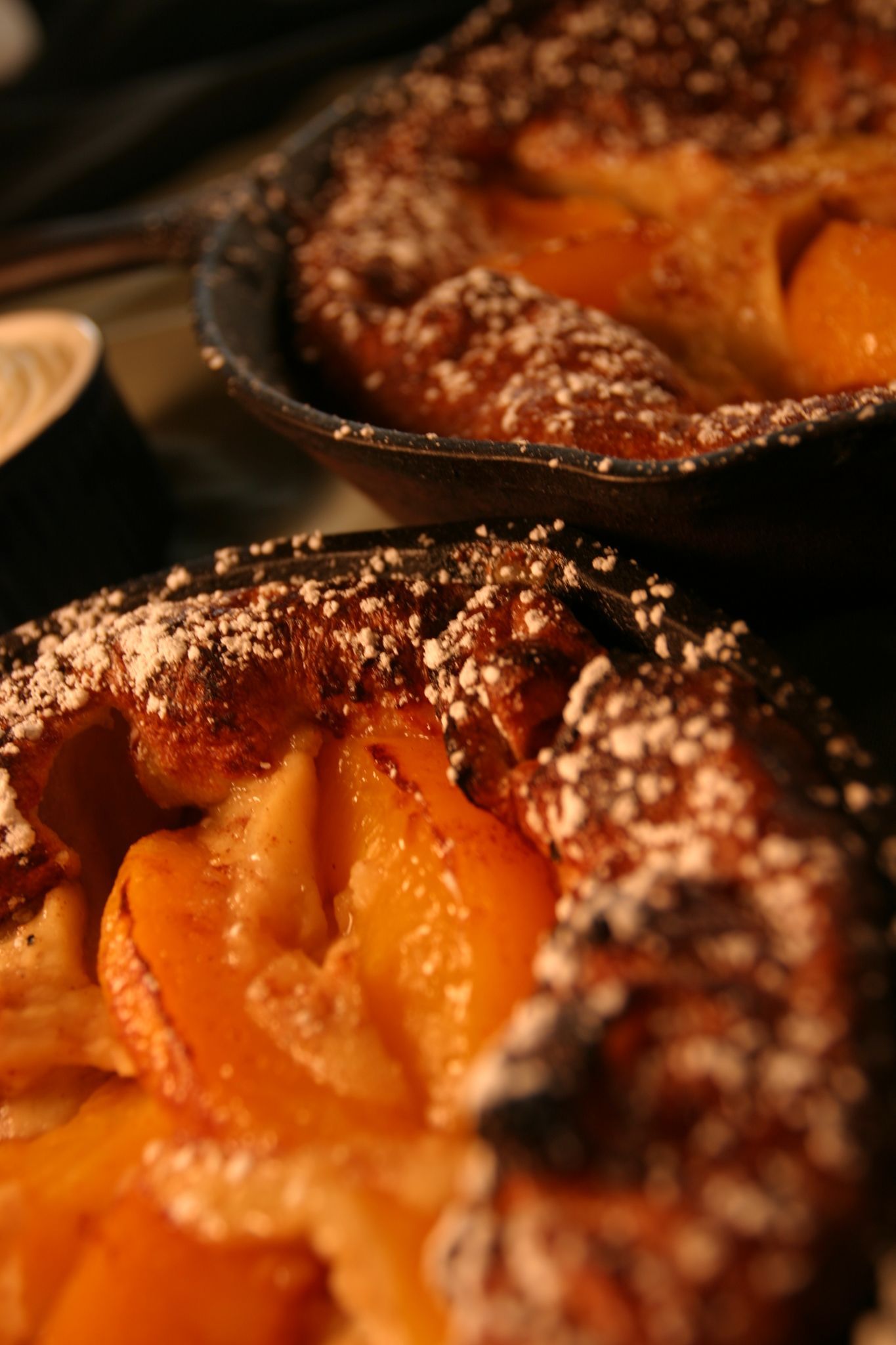 Peach pastries dusted with powdered sugar, in small iron skillets.