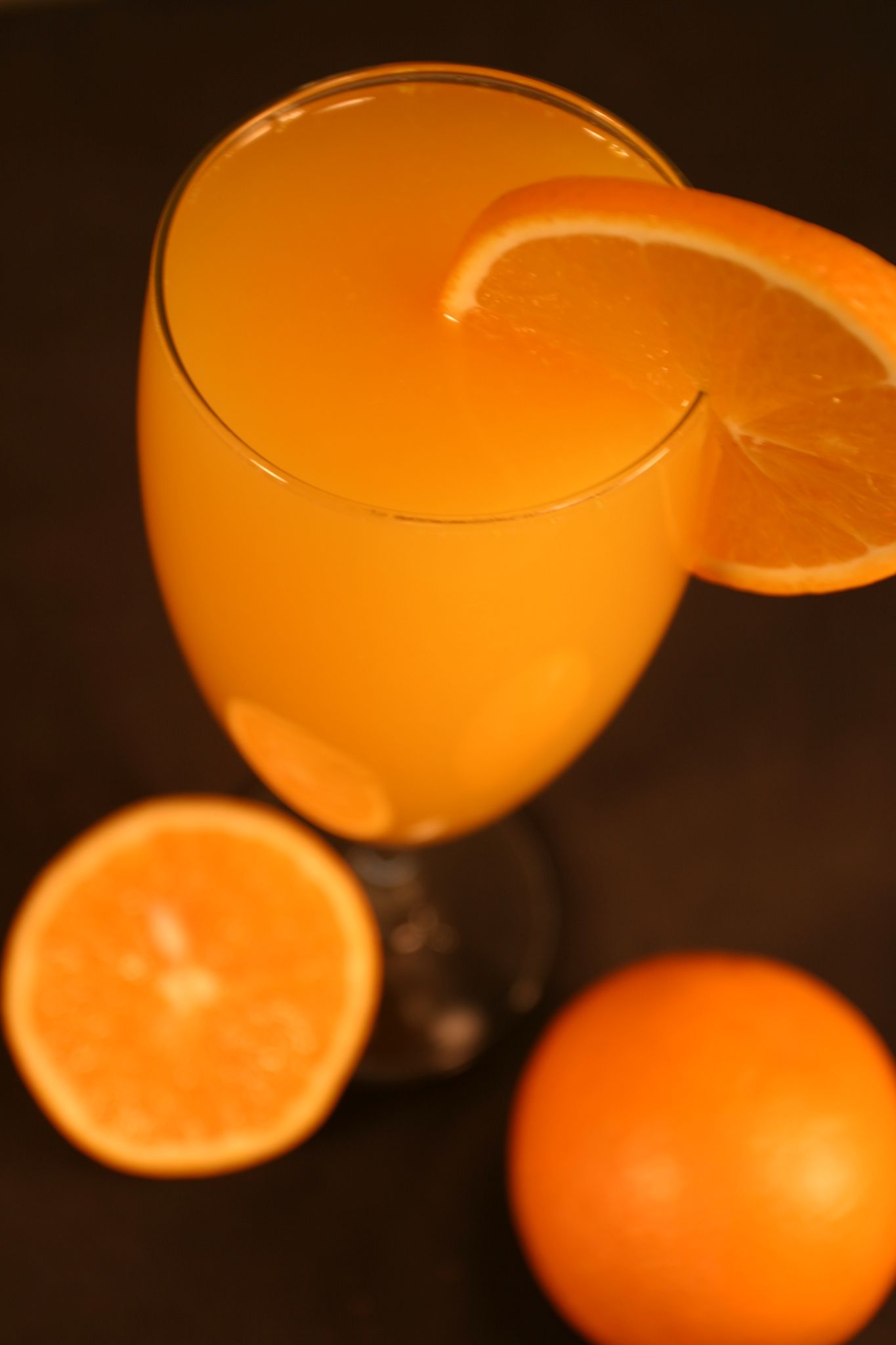 Orange juice in a glass, with an orange slice. Half an orange and a whole orange in view on a black surface.