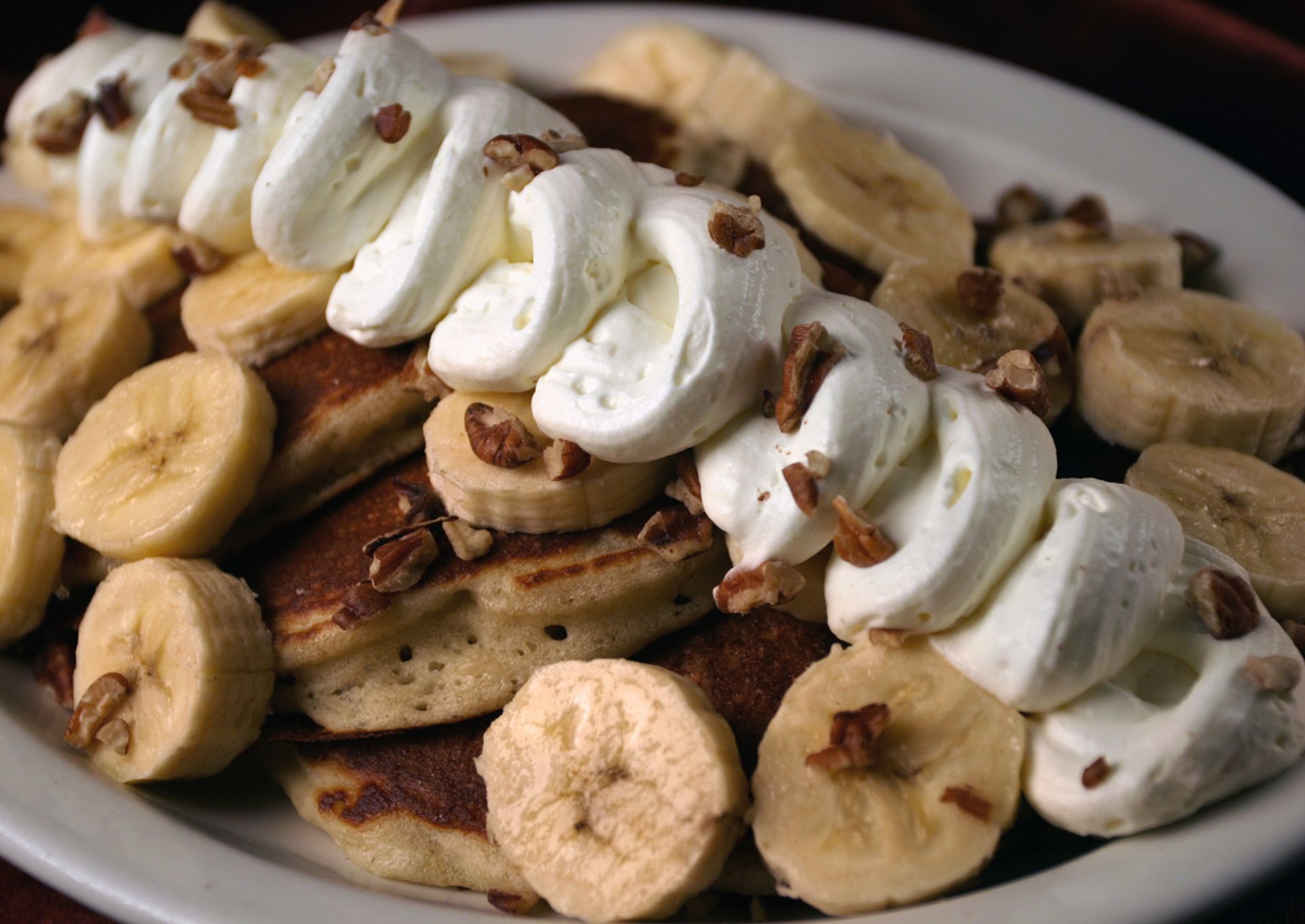 Pancakes topped with whipped cream, banana slices, and chopped nuts on a white plate.