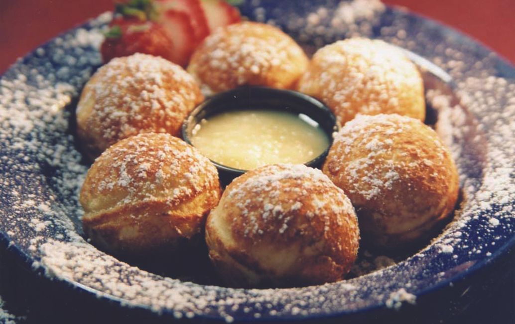 Aebleskivers, powdered with sugar, around a sauce and strawberry on a blue plate.