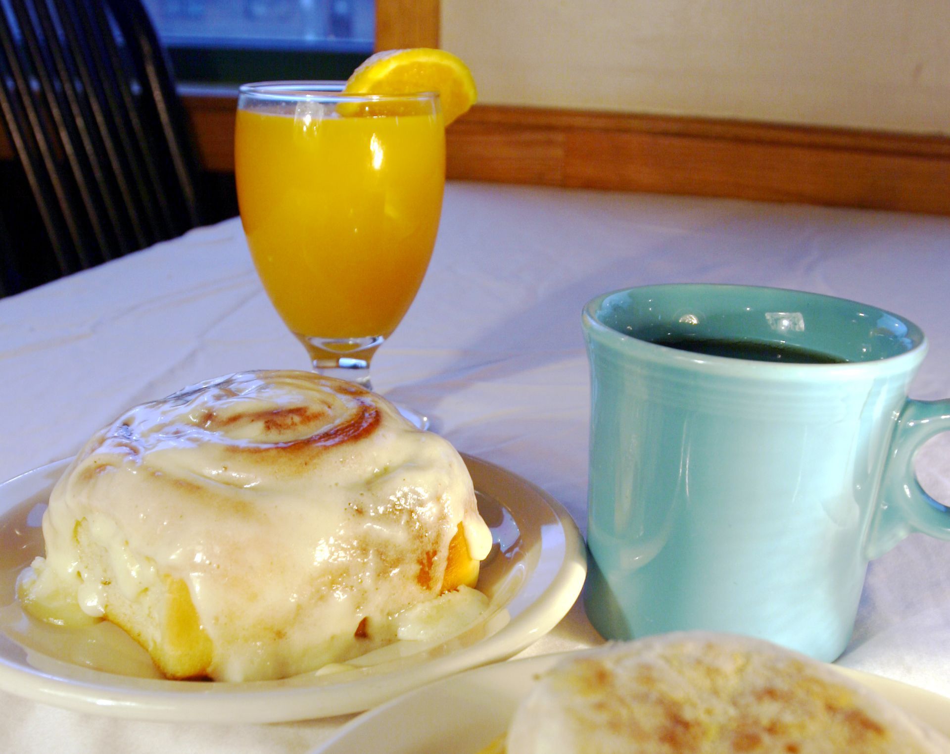 Breakfast: cinnamon roll, orange juice, coffee, and English muffin on a white tablecloth.