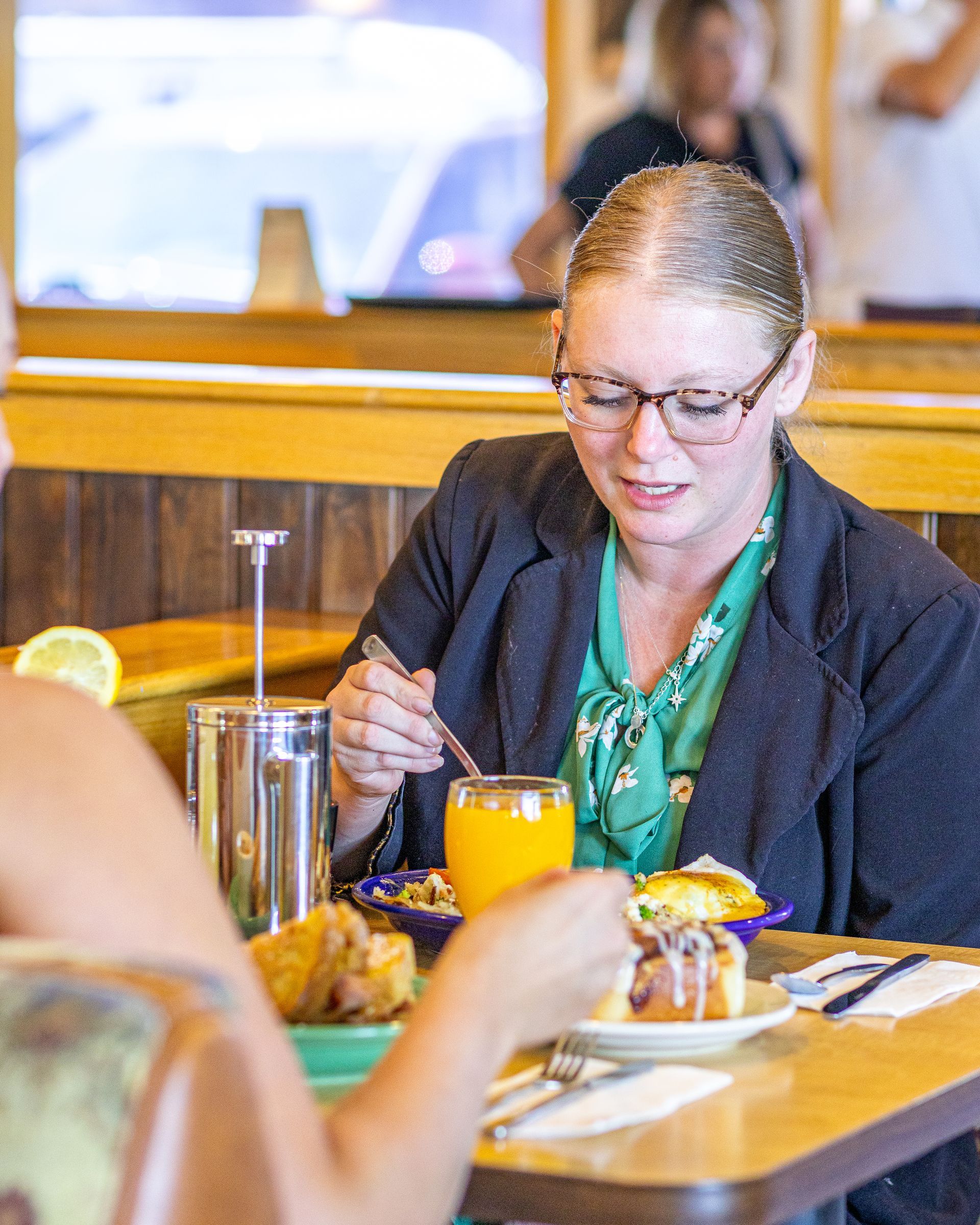 Woman in glasses eating at a restaurant table; orange juice and food on the table.