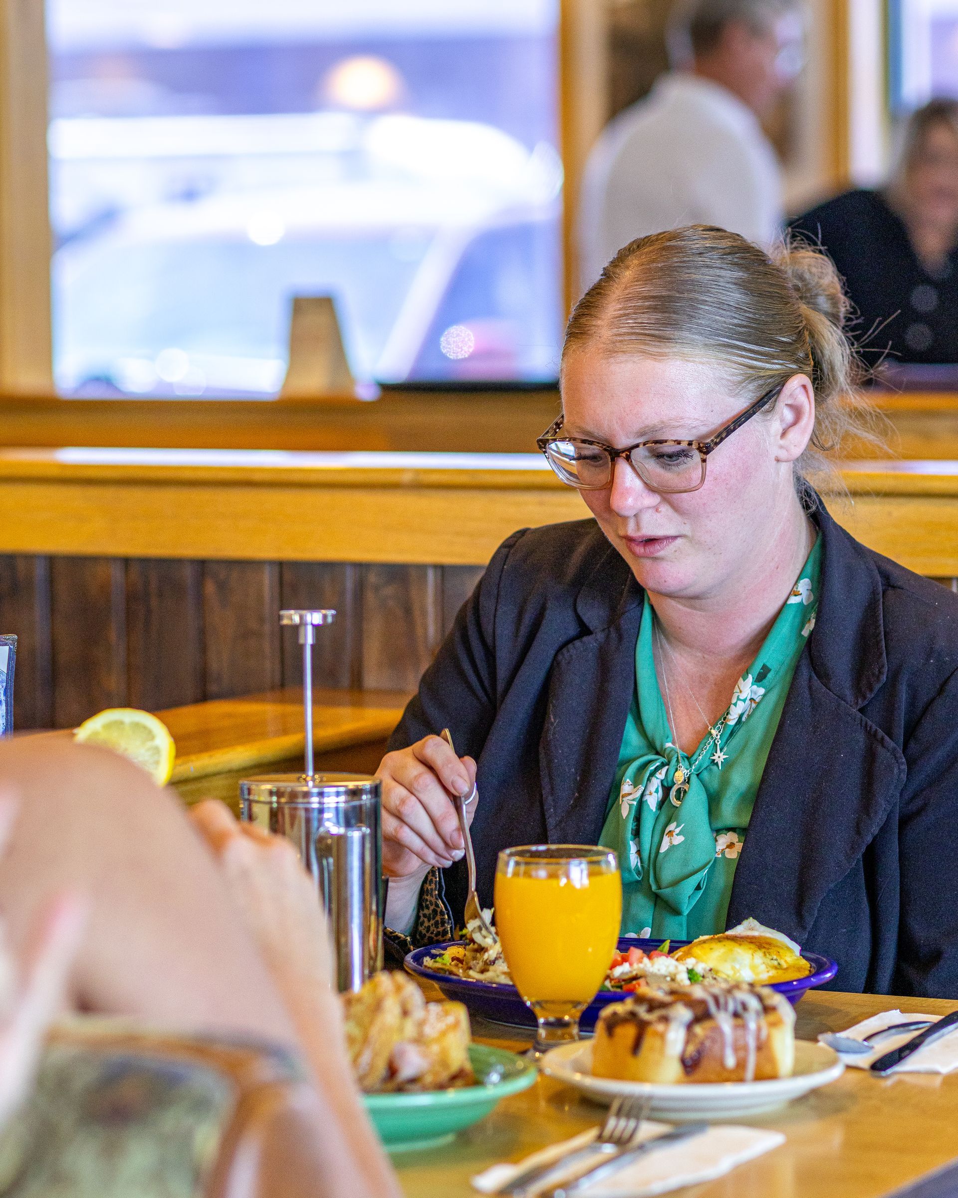 Woman in glasses eating breakfast at a restaurant, orange juice and cinnamon roll on the table.