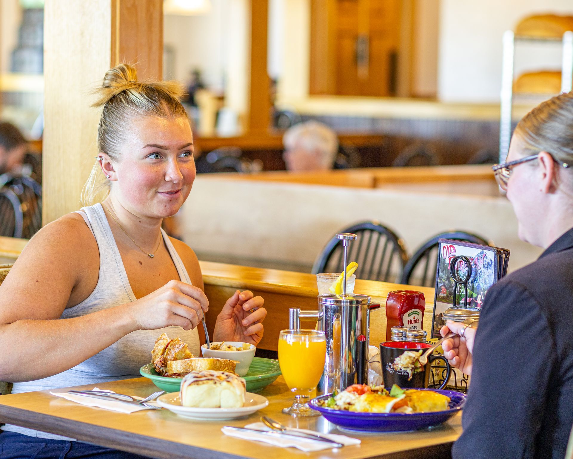 Two people eating and talking at a restaurant table with food and drinks.