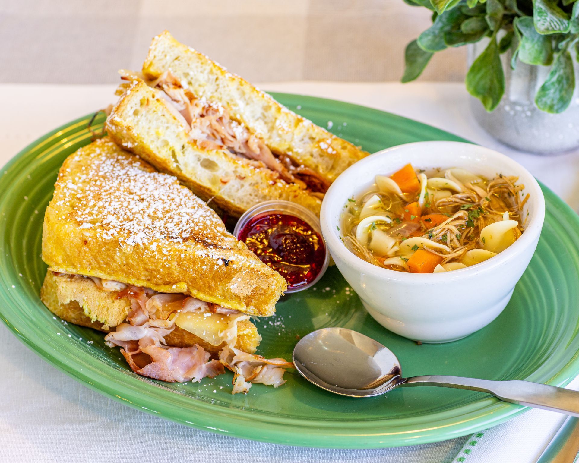 Grilled sandwich with filling, soup, and jam on a green plate.