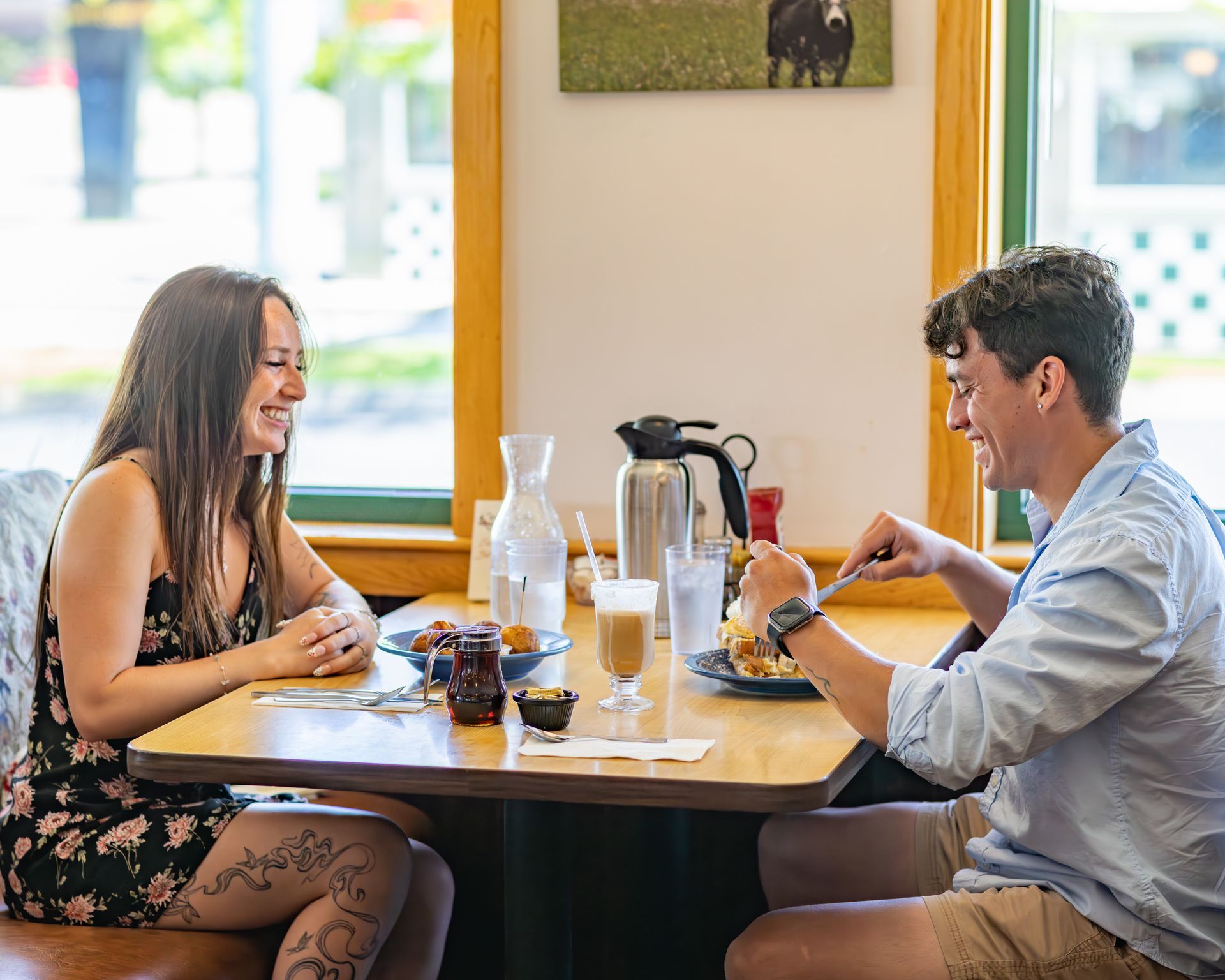 Woman and man laugh together at a diner booth, eating breakfast.