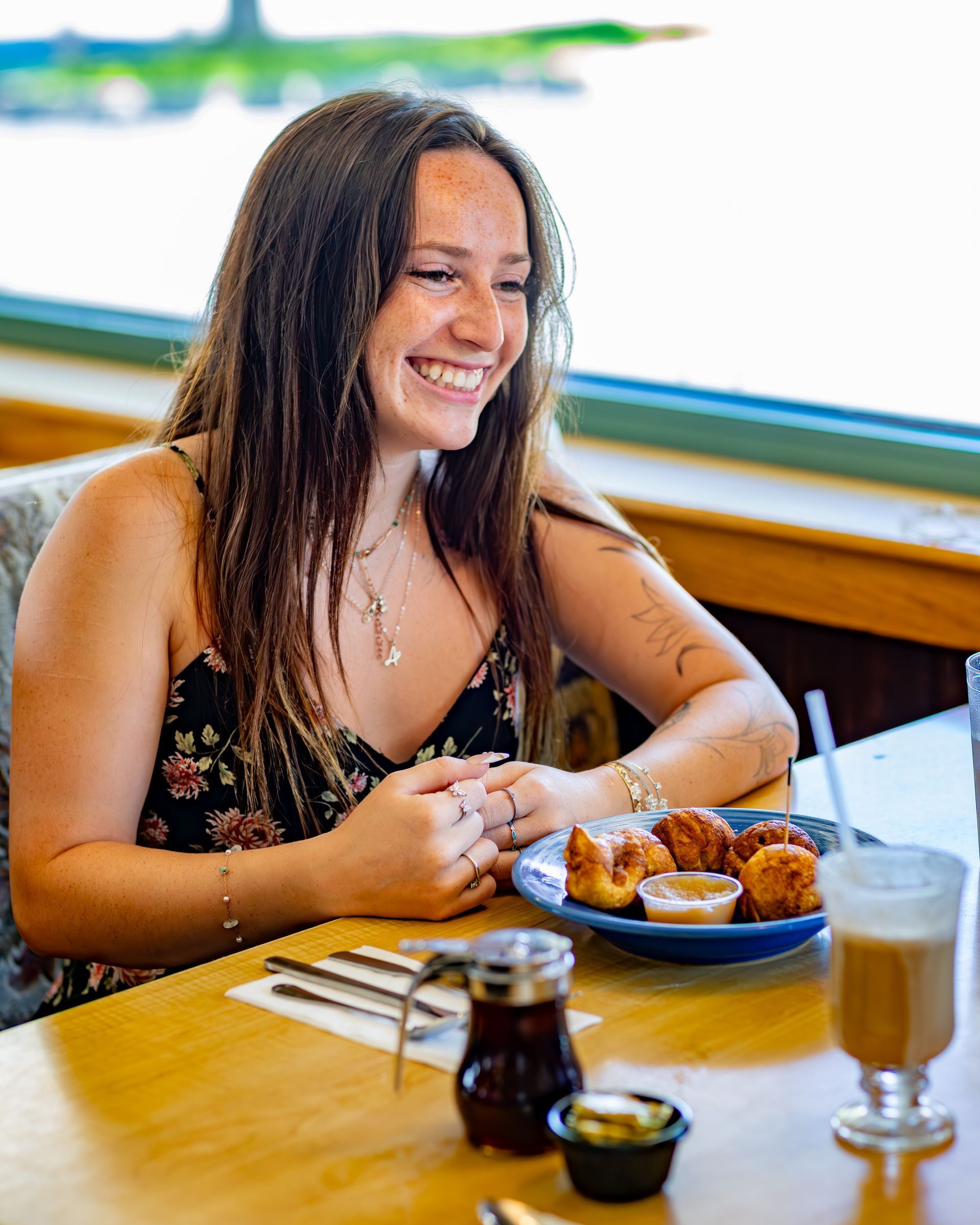 Woman smiling at a table with food, coffee, and syrup in a restaurant.