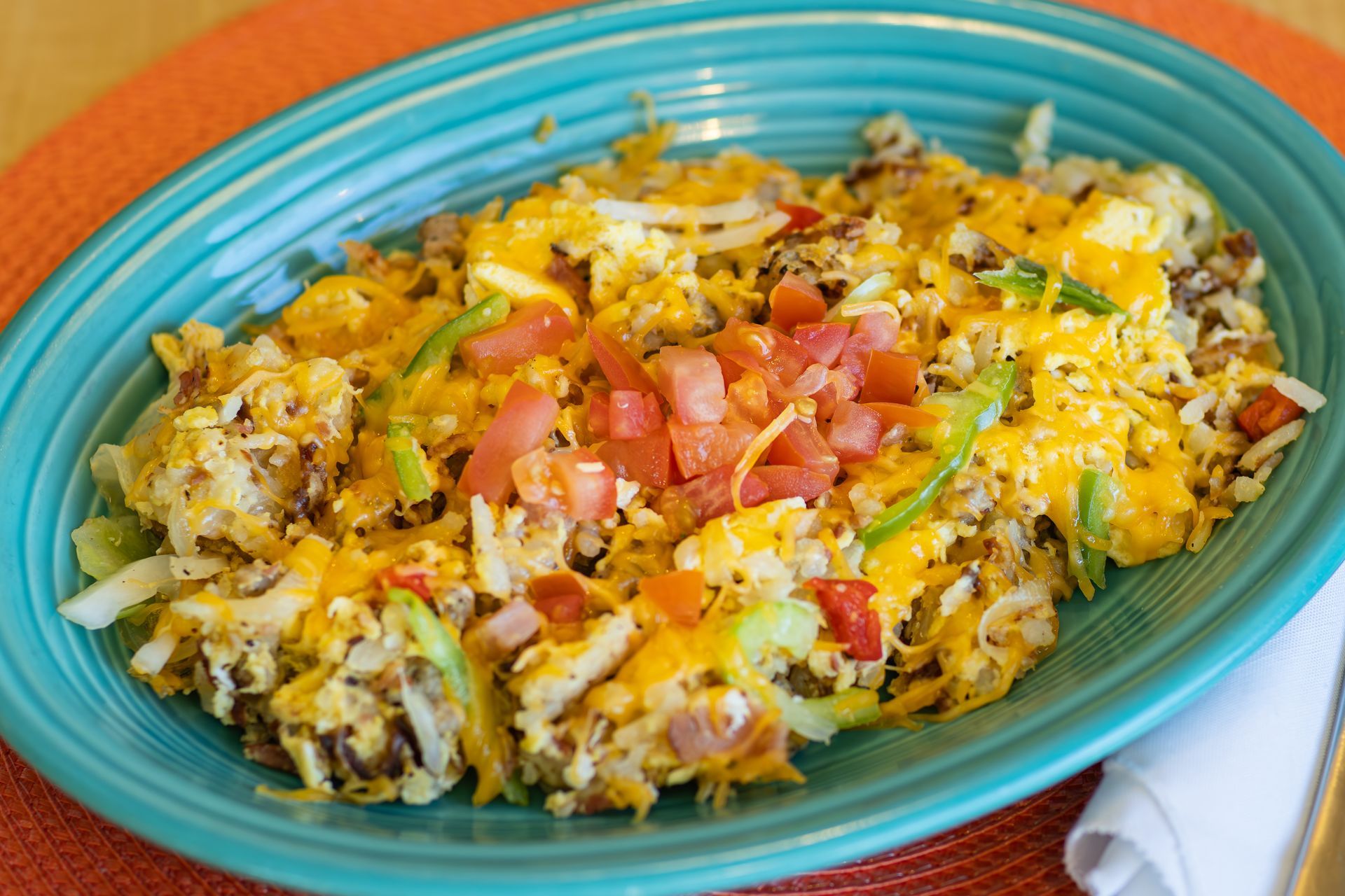 Hash with cheese, tomatoes, peppers, and onions on a blue platter.