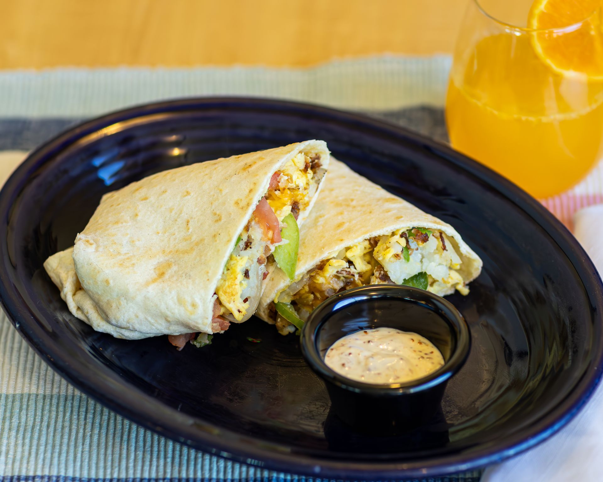 Breakfast burrito cut in half with a small side of sauce and a glass of orange juice.