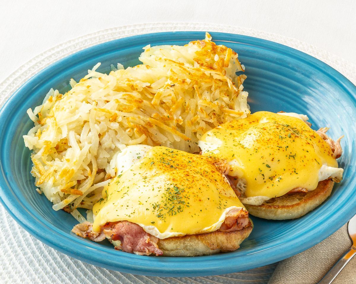 Eggs Benedict with hash browns on a blue plate.