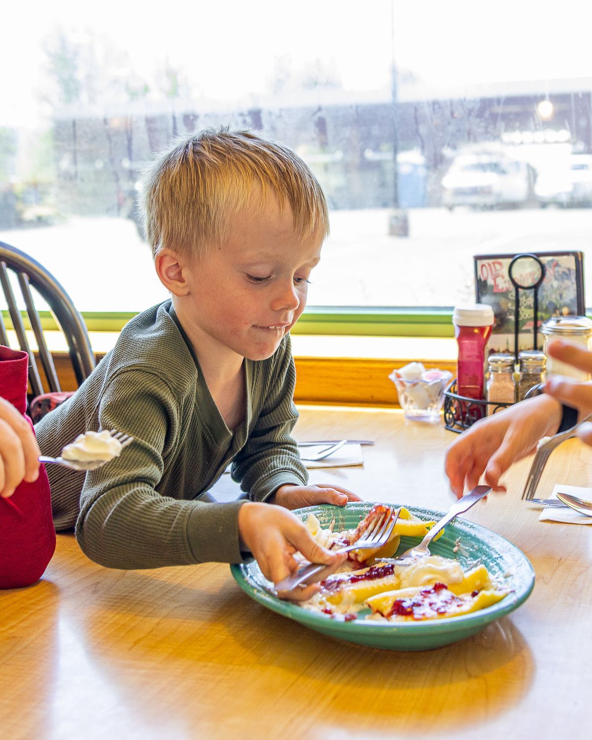 Young child at a table eating from a plate of food. The child is reaching for food with a fork.