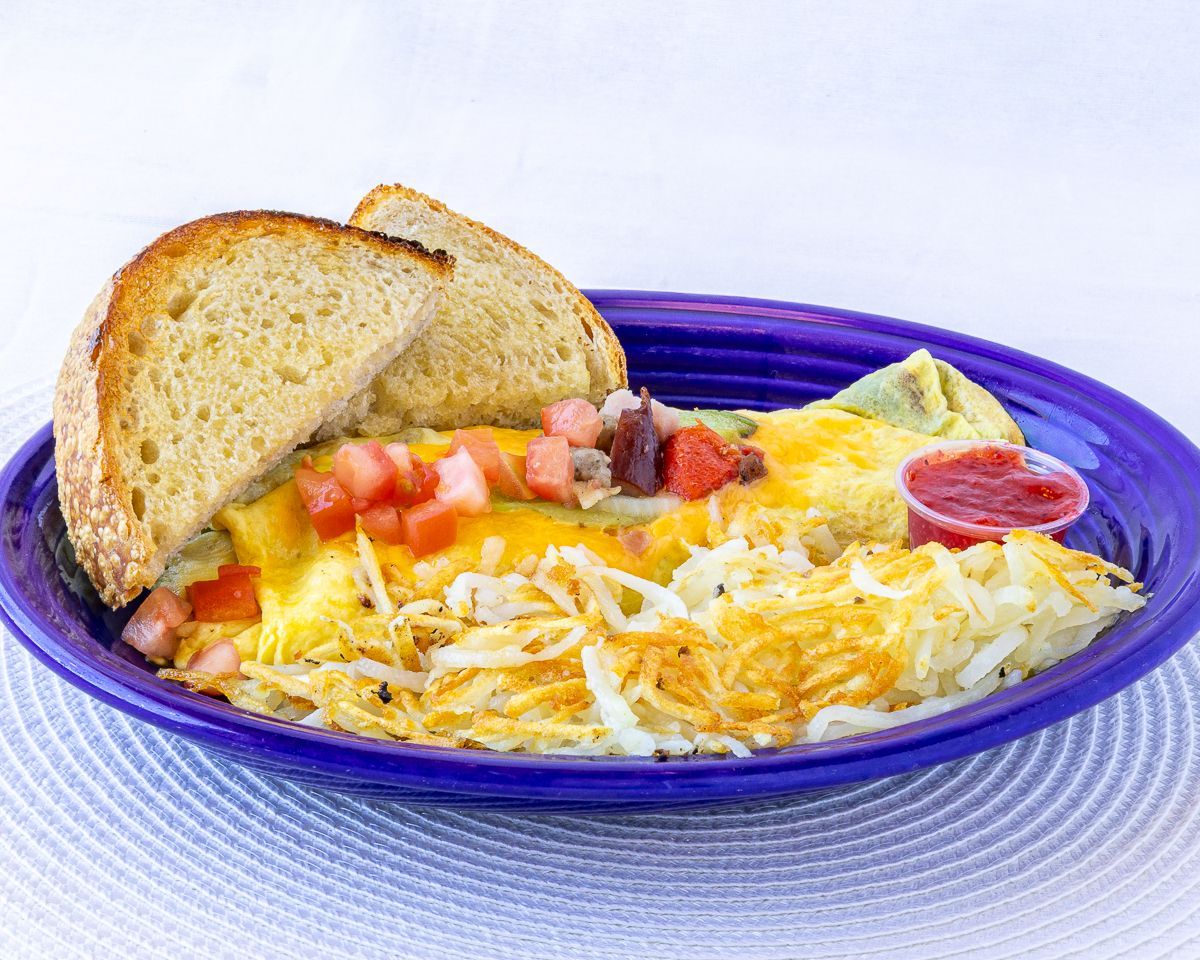 Omelet with diced tomatoes, cheese, hash browns, toast, and a side of red sauce on a purple plate.