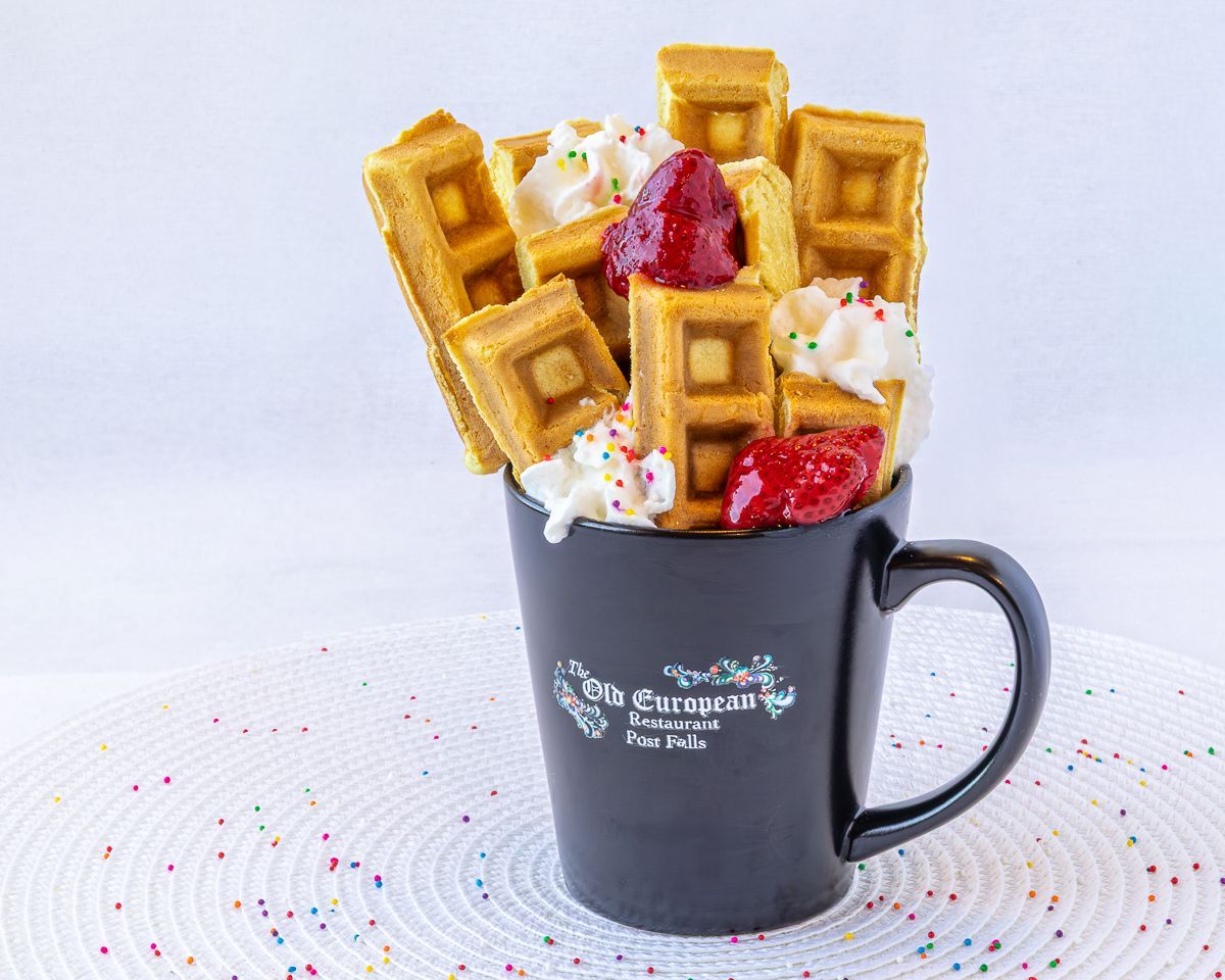 Waffles with whipped cream and strawberries, arranged in a black mug.