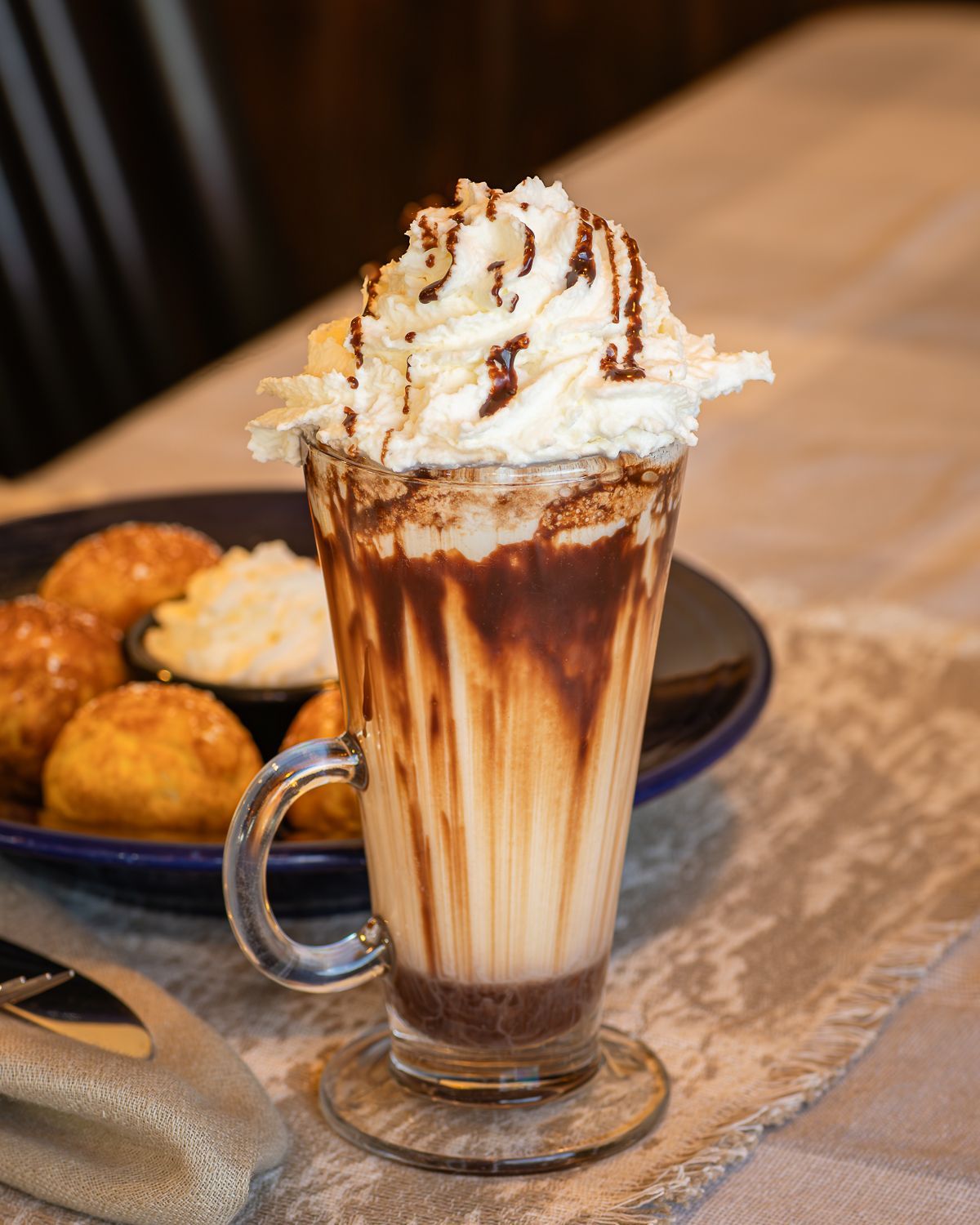 Chocolate dessert beverage with whipped cream and drizzle. Donuts and dipping sauce on a blue plate.