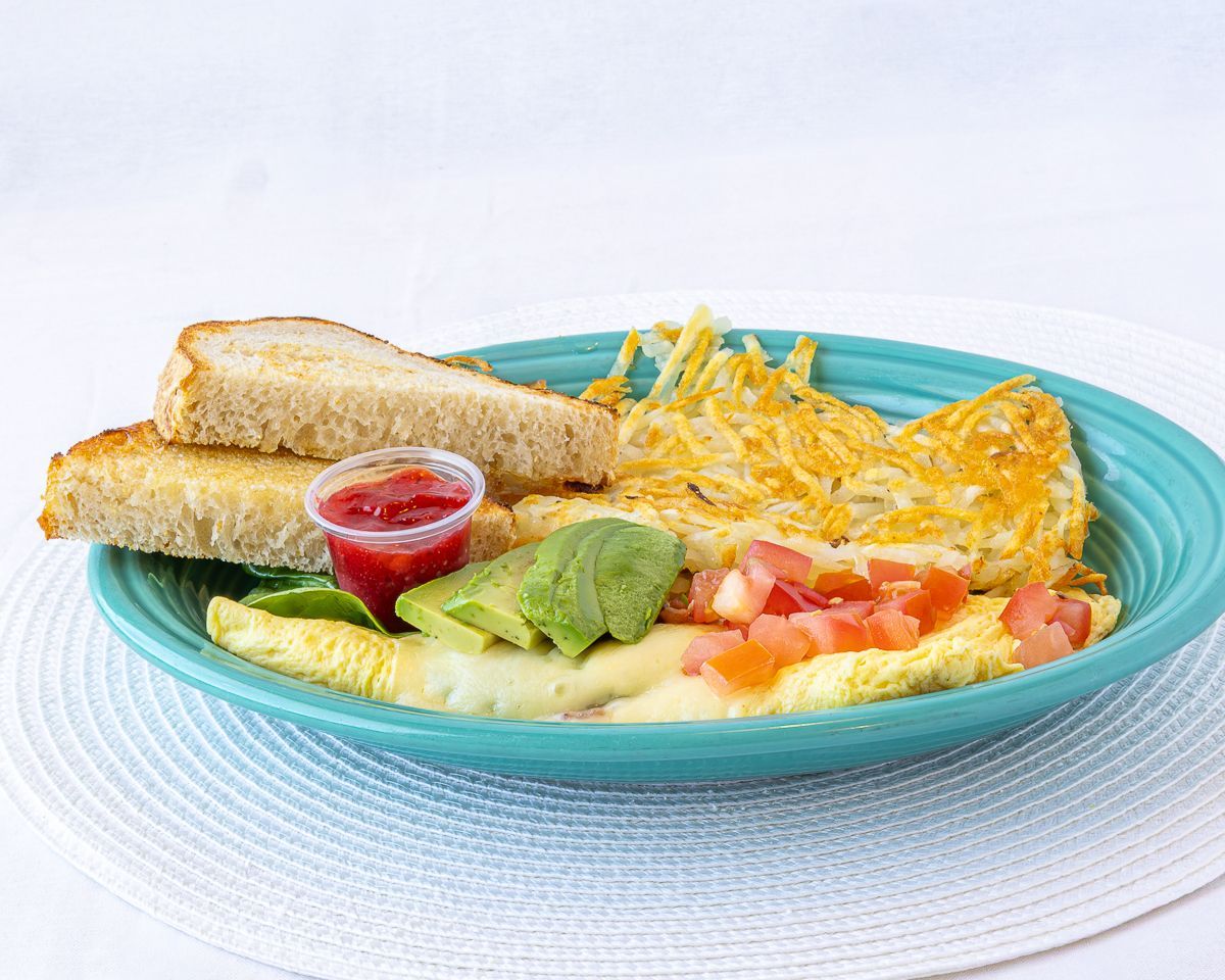 Omelet with avocado, diced tomatoes, hash browns, and toast on a teal plate.