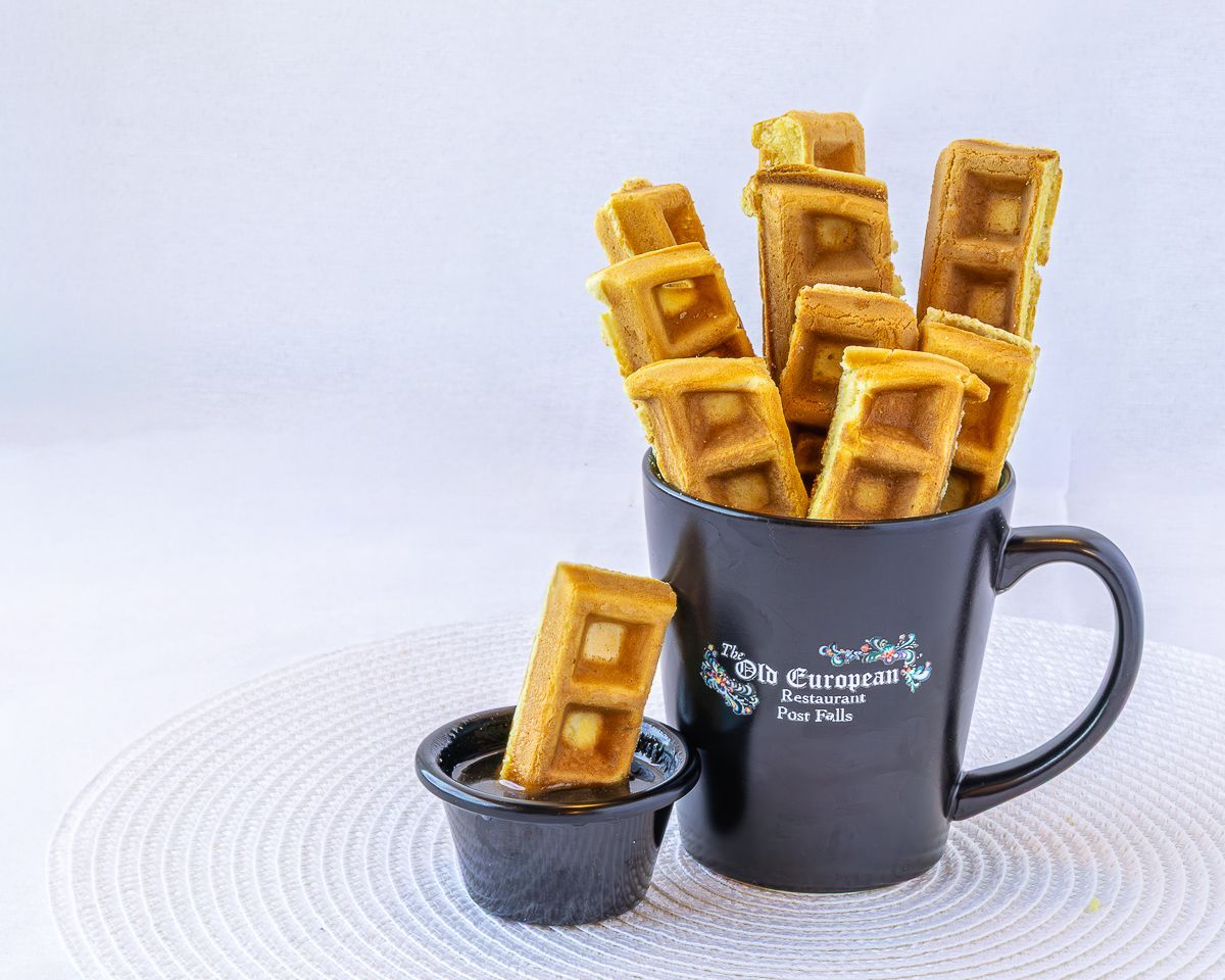 Waffle sticks in a black mug, with one dipped in a small dish, on a white mat.