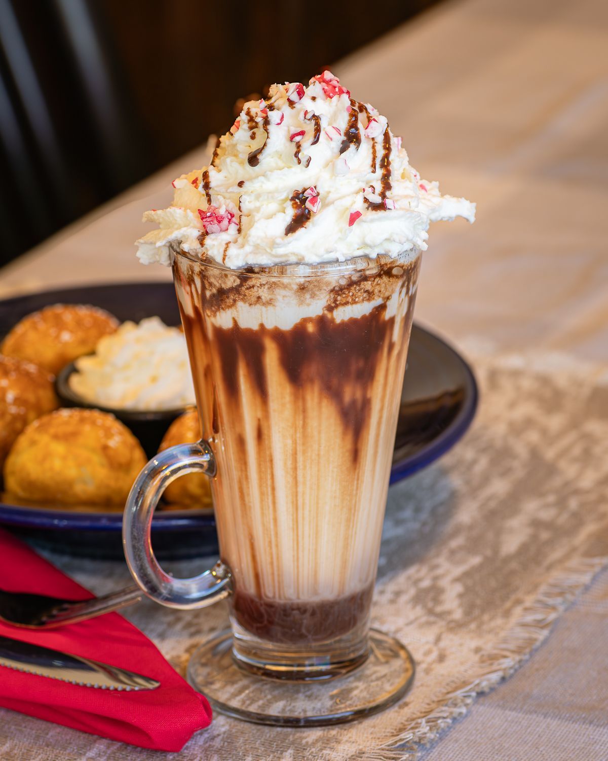 Tall glass of layered drink topped with whipped cream, chocolate drizzle, and candy cane pieces.