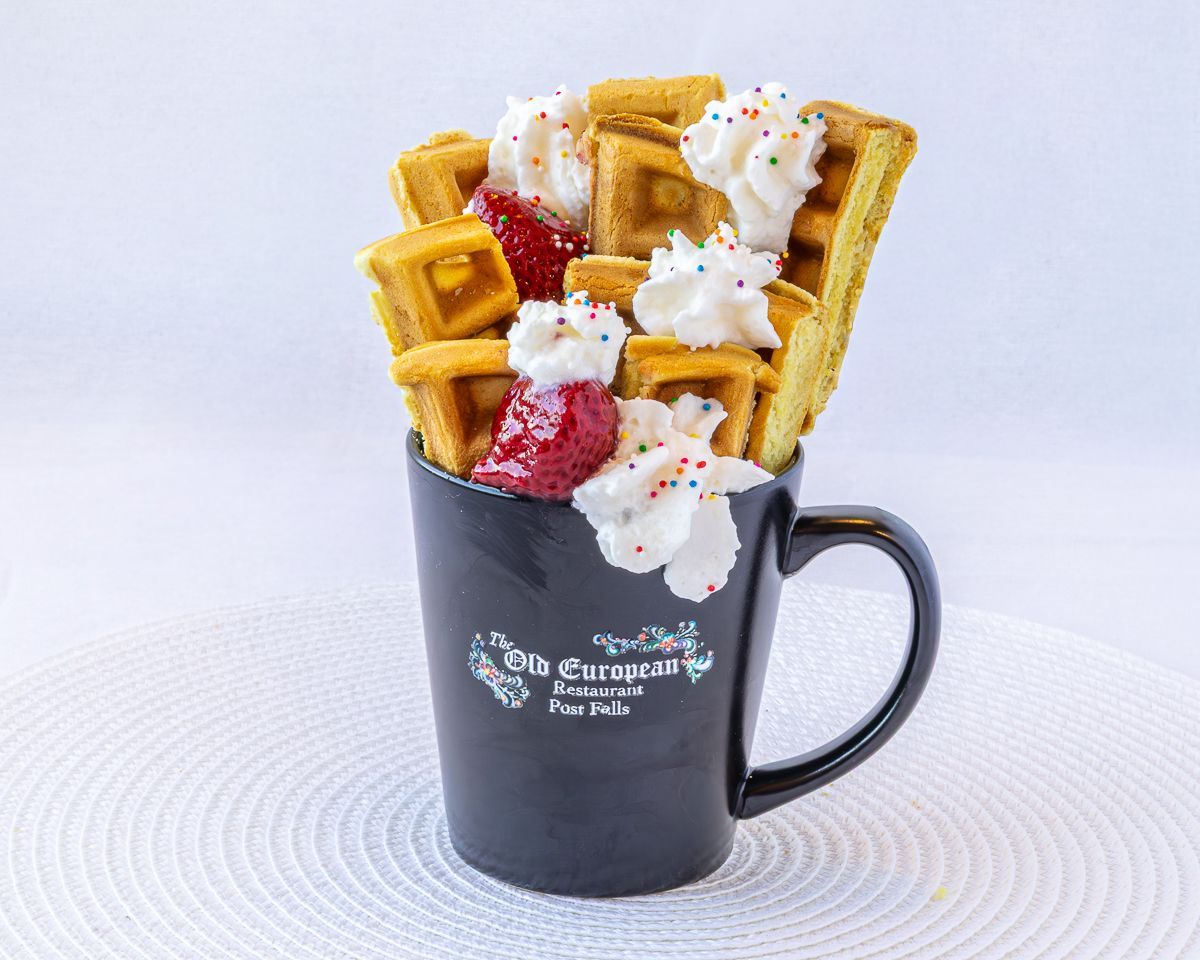 Waffles with whipped cream and strawberries in a black mug.