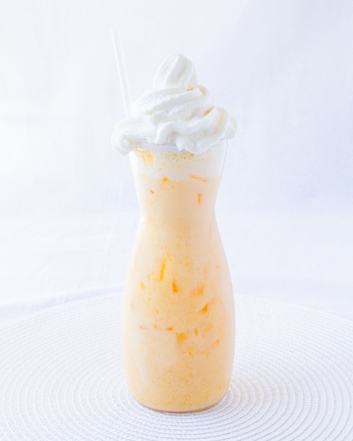 Orange milkshake with whipped cream topping in hourglass-shaped glass with a straw.
