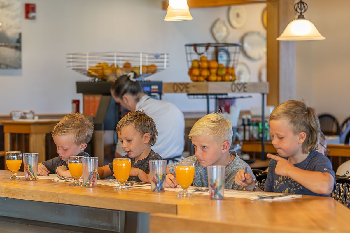 Four children at a diner counter, each with a glass of orange juice. A server is behind them.