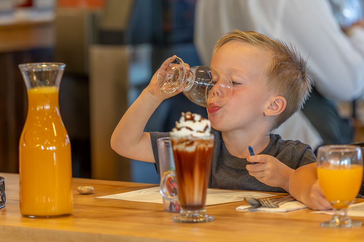 Boy drinking from a glass, orange juice and a shake on the table.