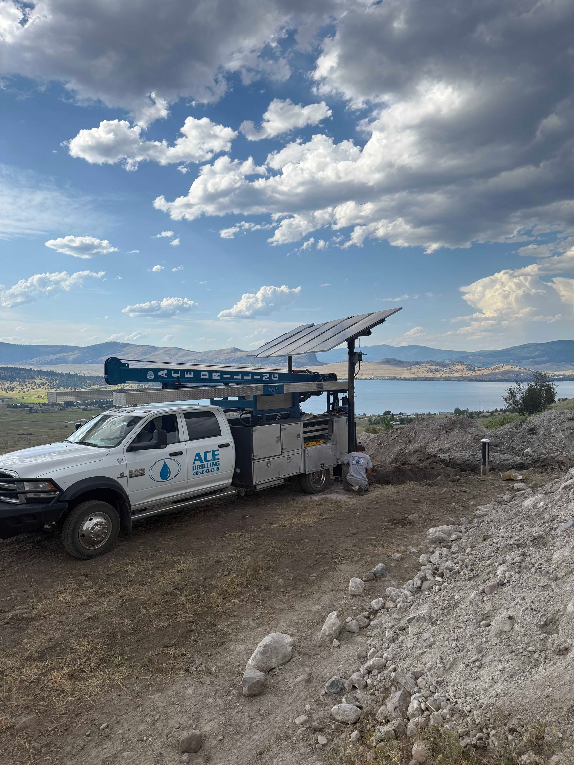 White truck towing a trailer with solar panels. Overlooks a lake under a cloudy sky.