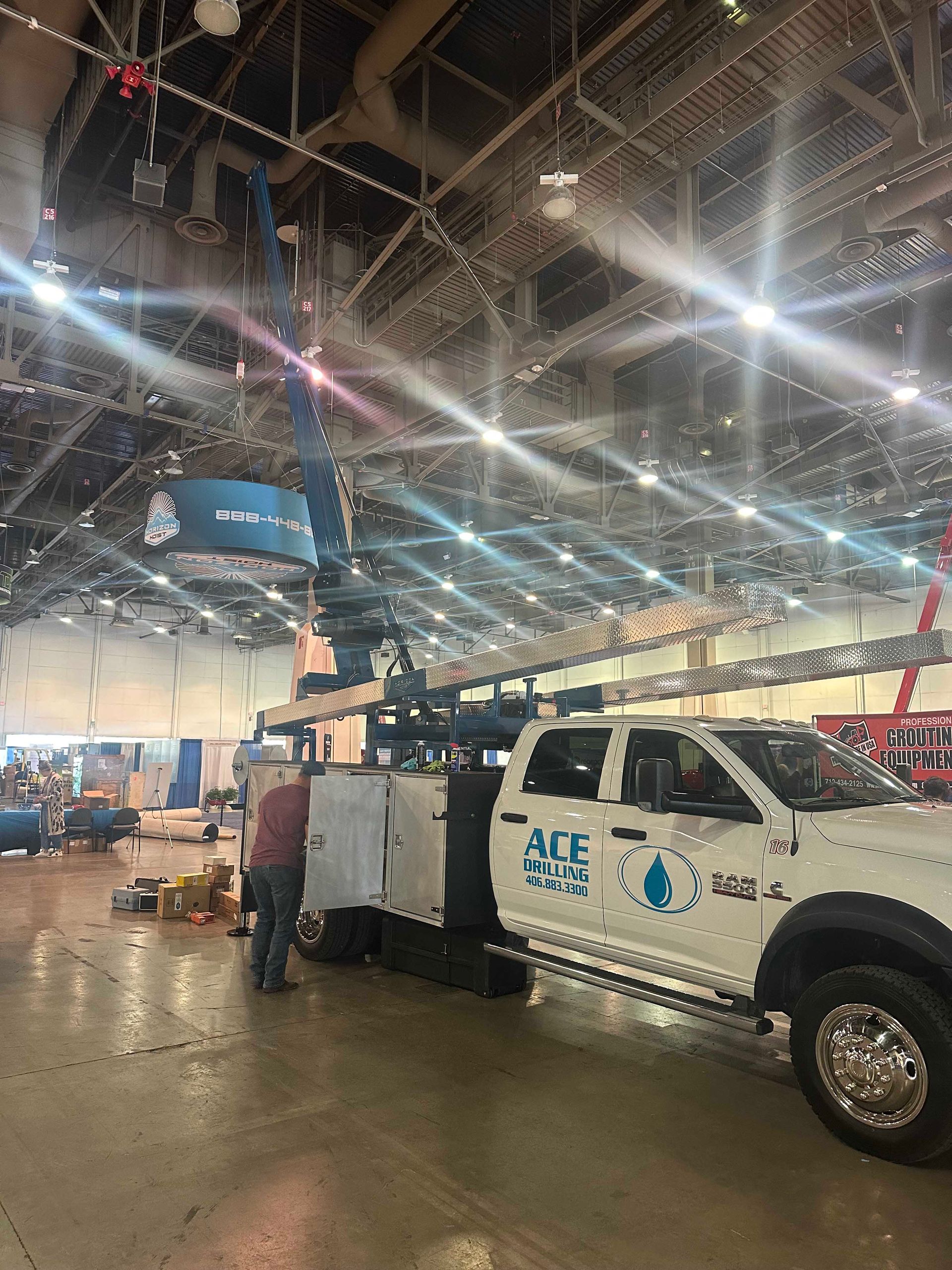 White service truck with raised crane inside a large building; person stands nearby.