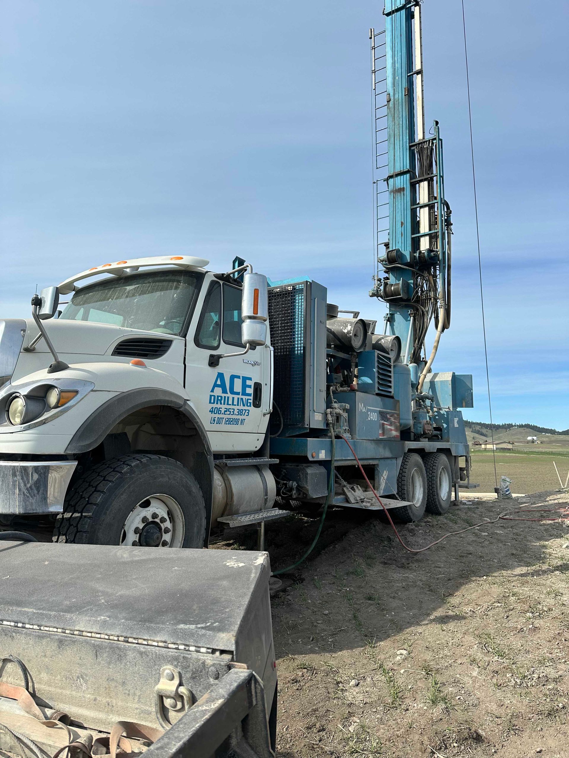 Blue well drilling truck with tall rig, parked on dirt. 
