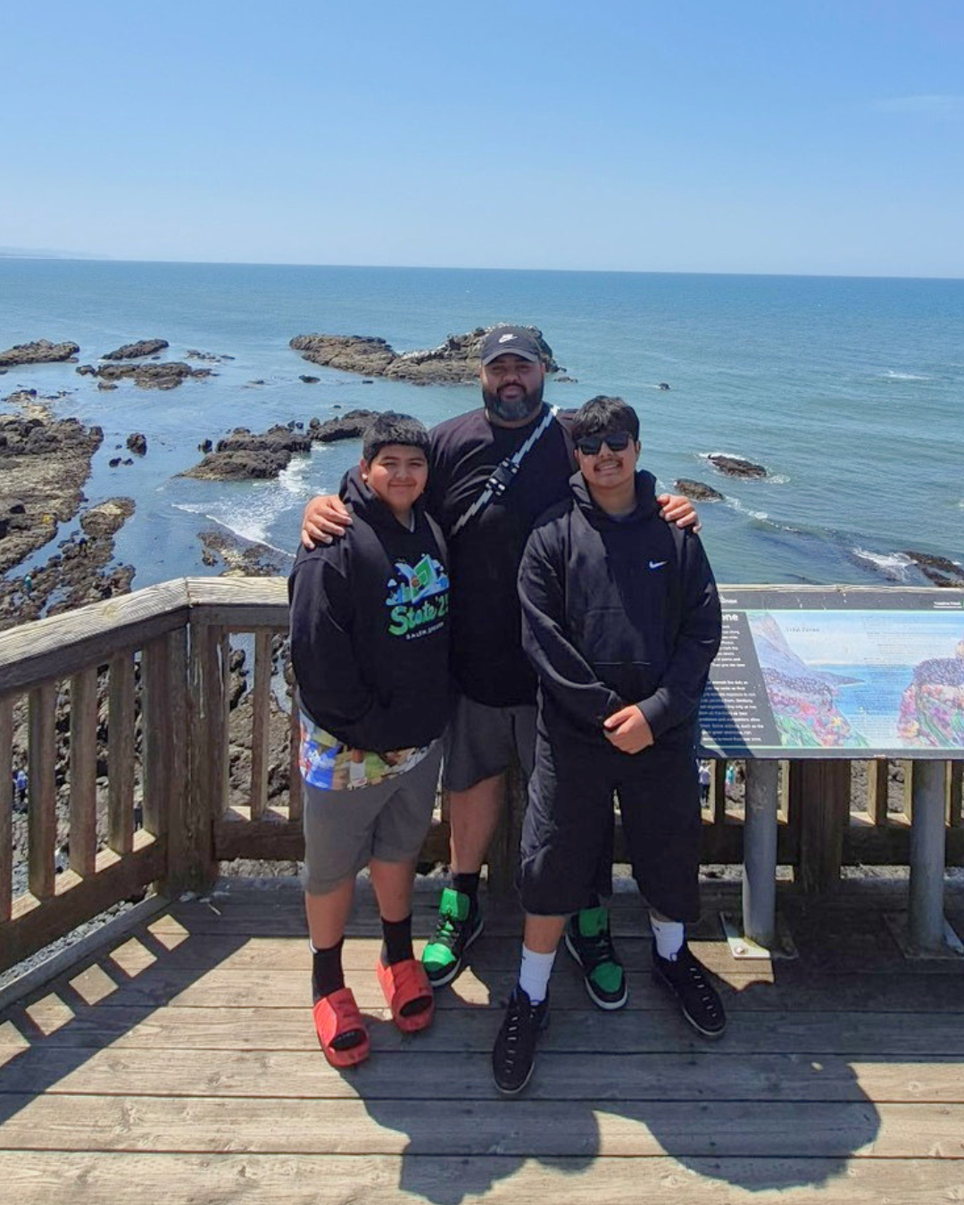 Three people posing on a wooden lookout deck by the ocean on a sunny day.