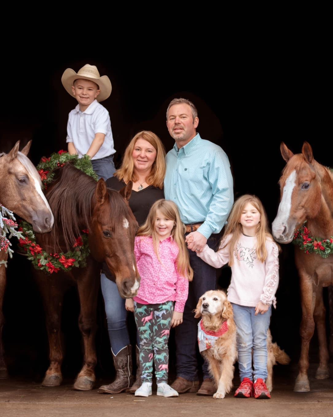 A family is posing for a picture with horses and a dog.