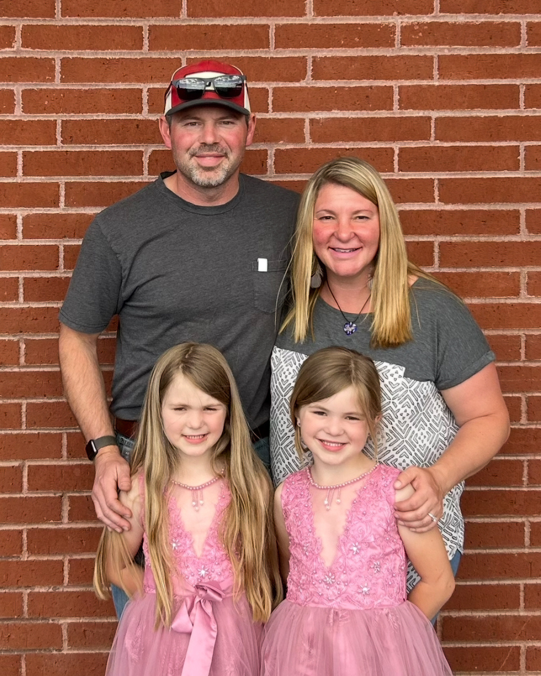 A family is posing for a picture in front of a brick wall.