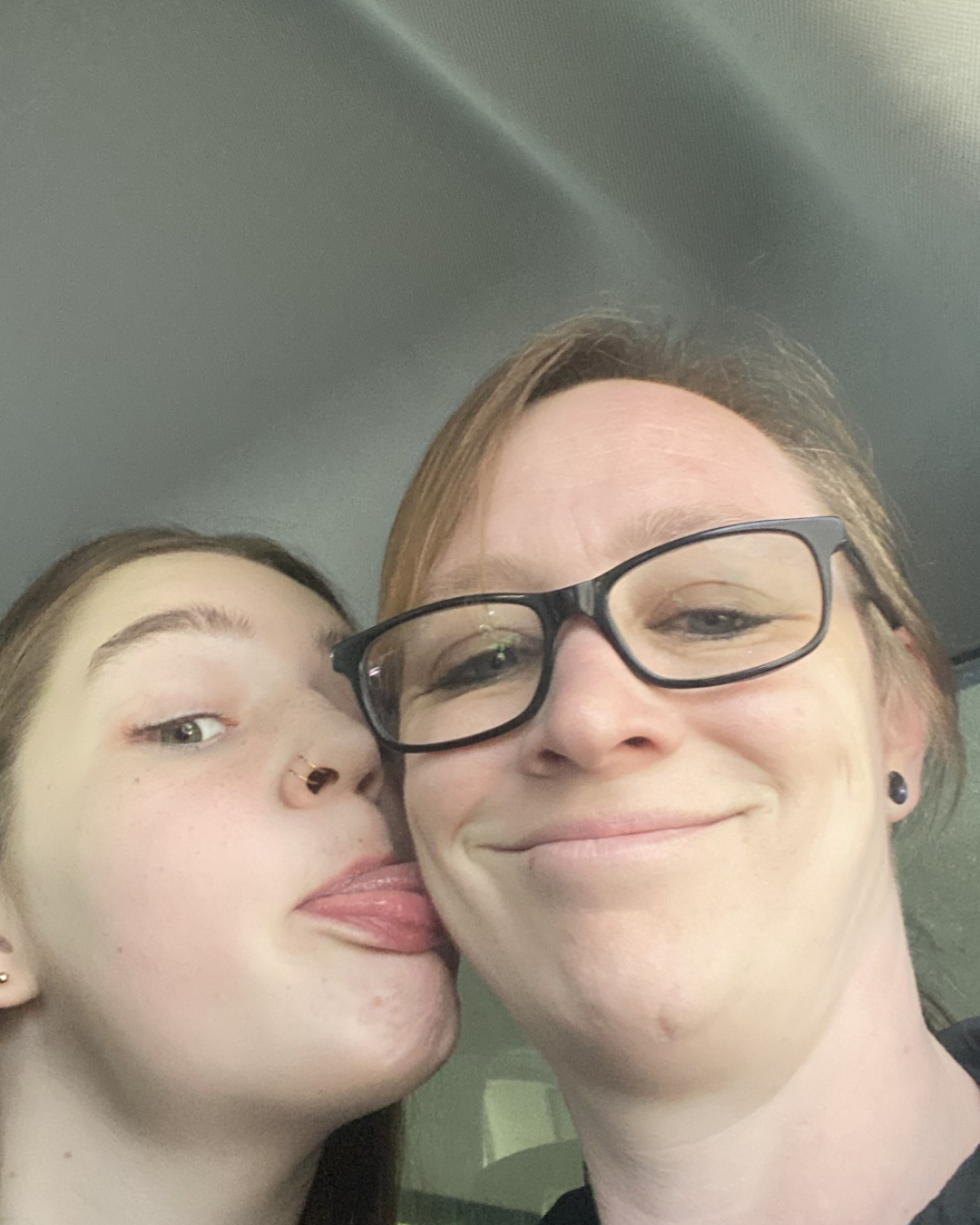 A woman wearing glasses is kissing a girl on the cheek.