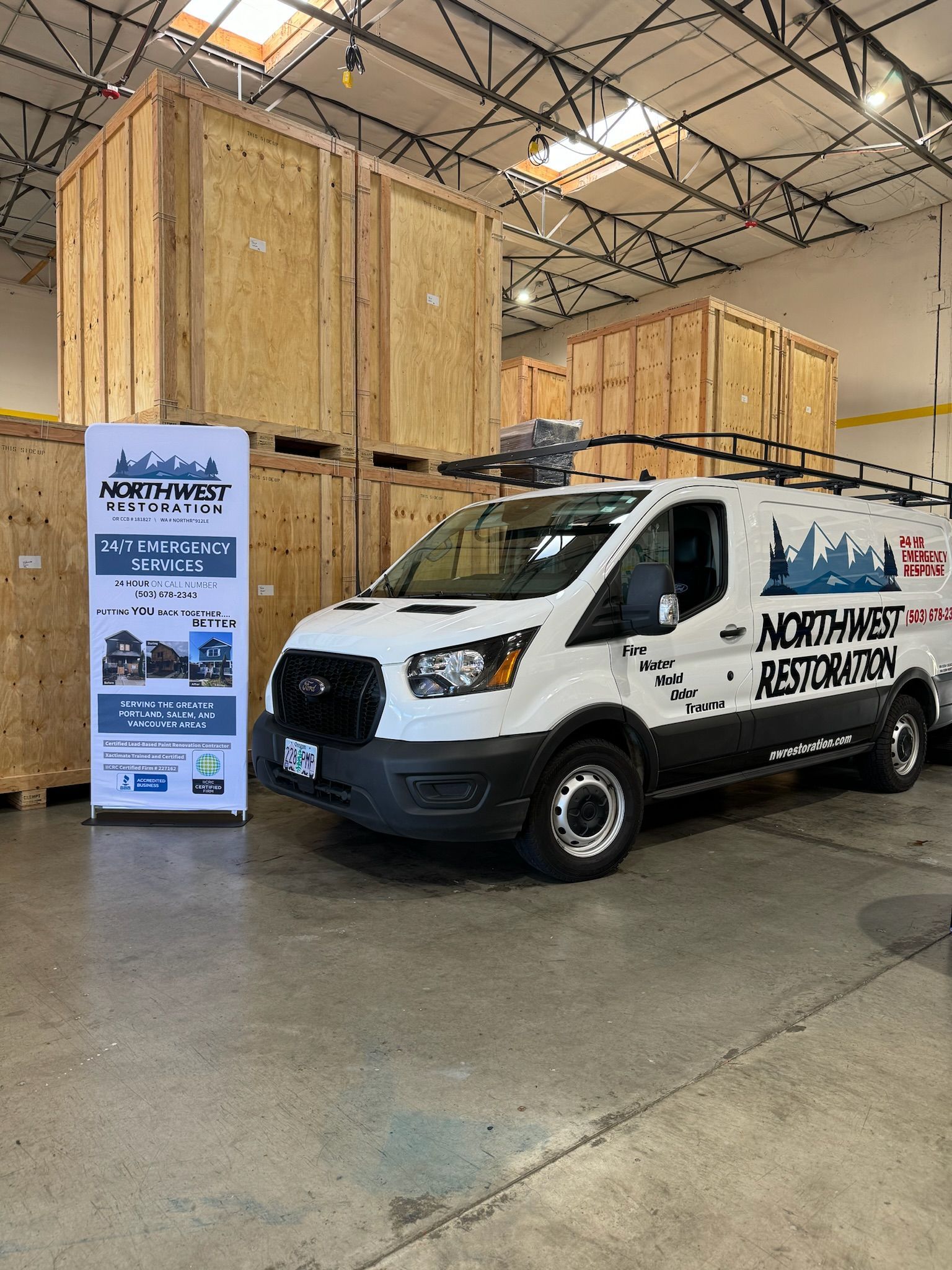 White van with logo parked in warehouse near wooden crates and a banner.