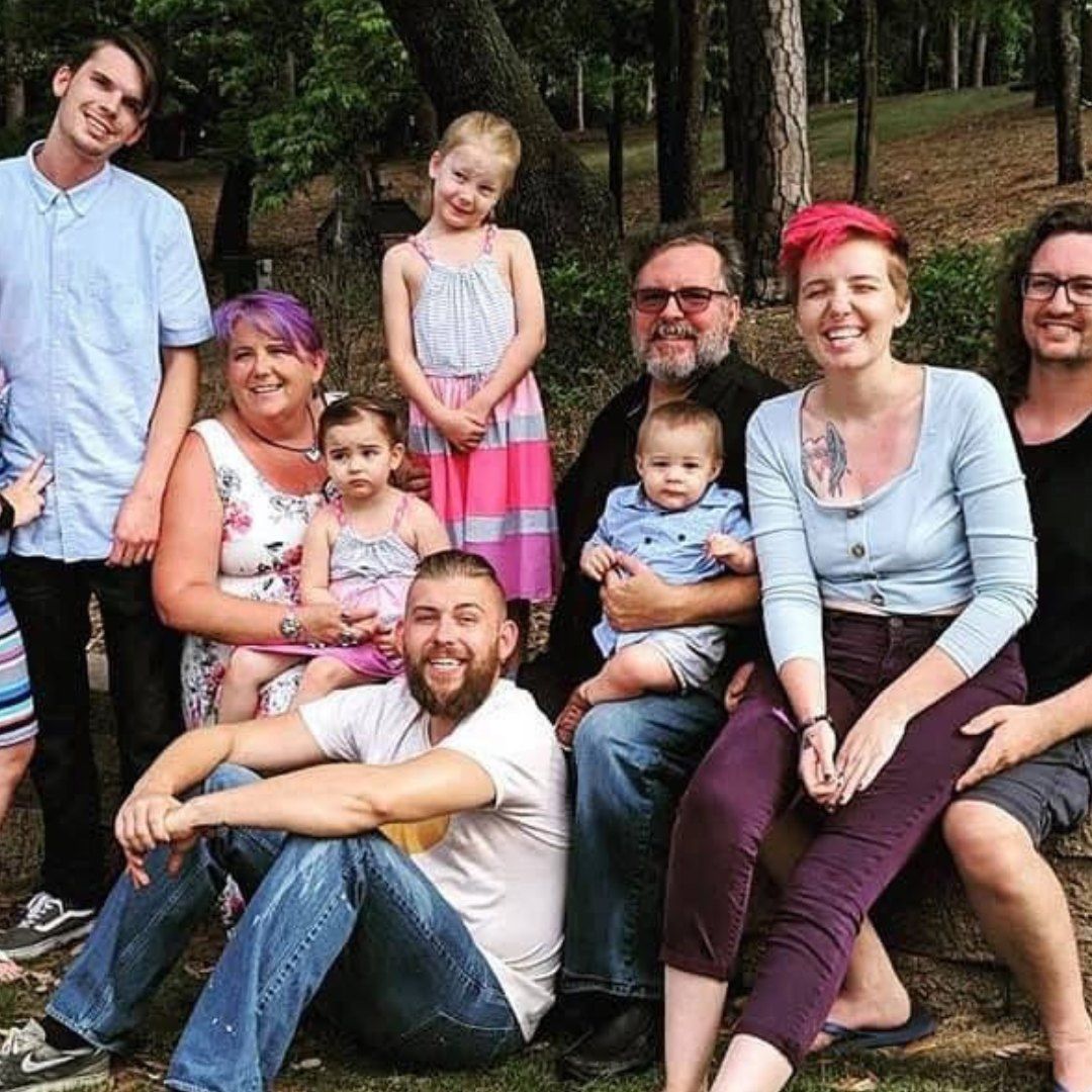 A large family is posing for a picture in the woods.