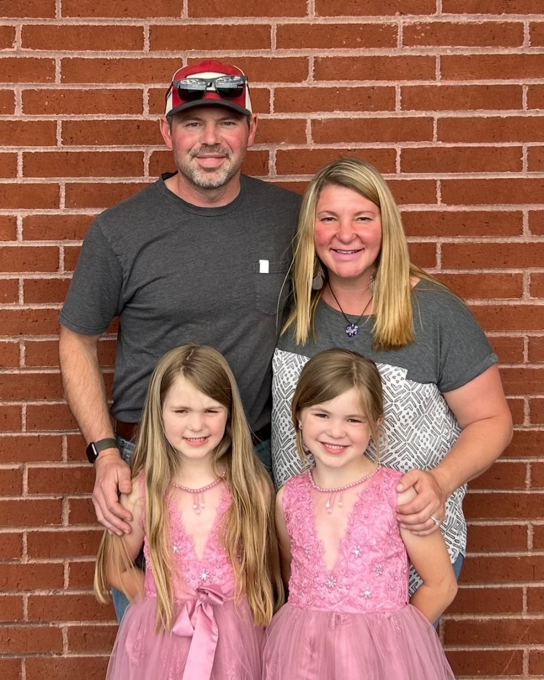 Family of four poses in front of a brick wall