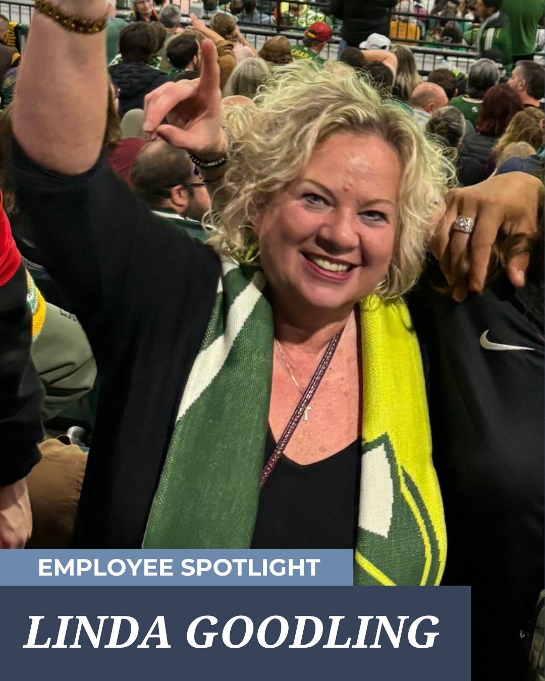 Woman in Packers scarf at game, smiling, holding up a finger, in crowd