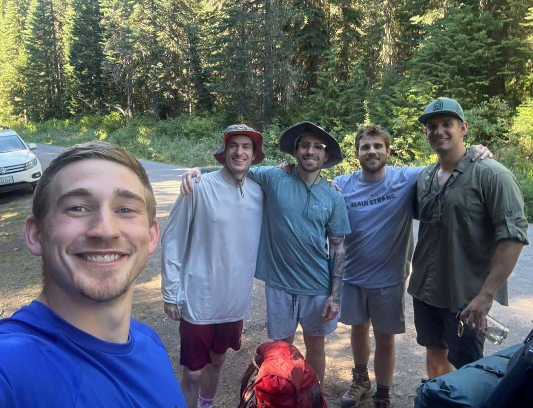 Five people smile while posing for a group selfie on a paved path in a forest clearing. 