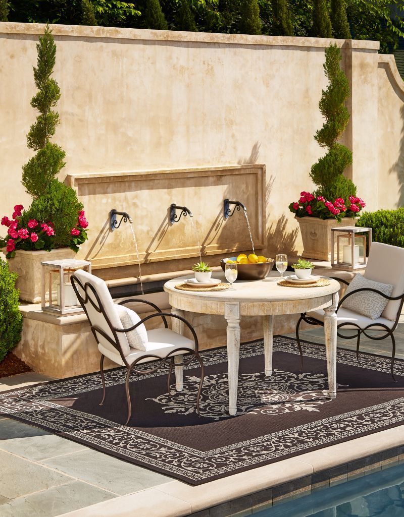 Outdoor dining area with fountain, round table, chairs, rug, and potted plants.