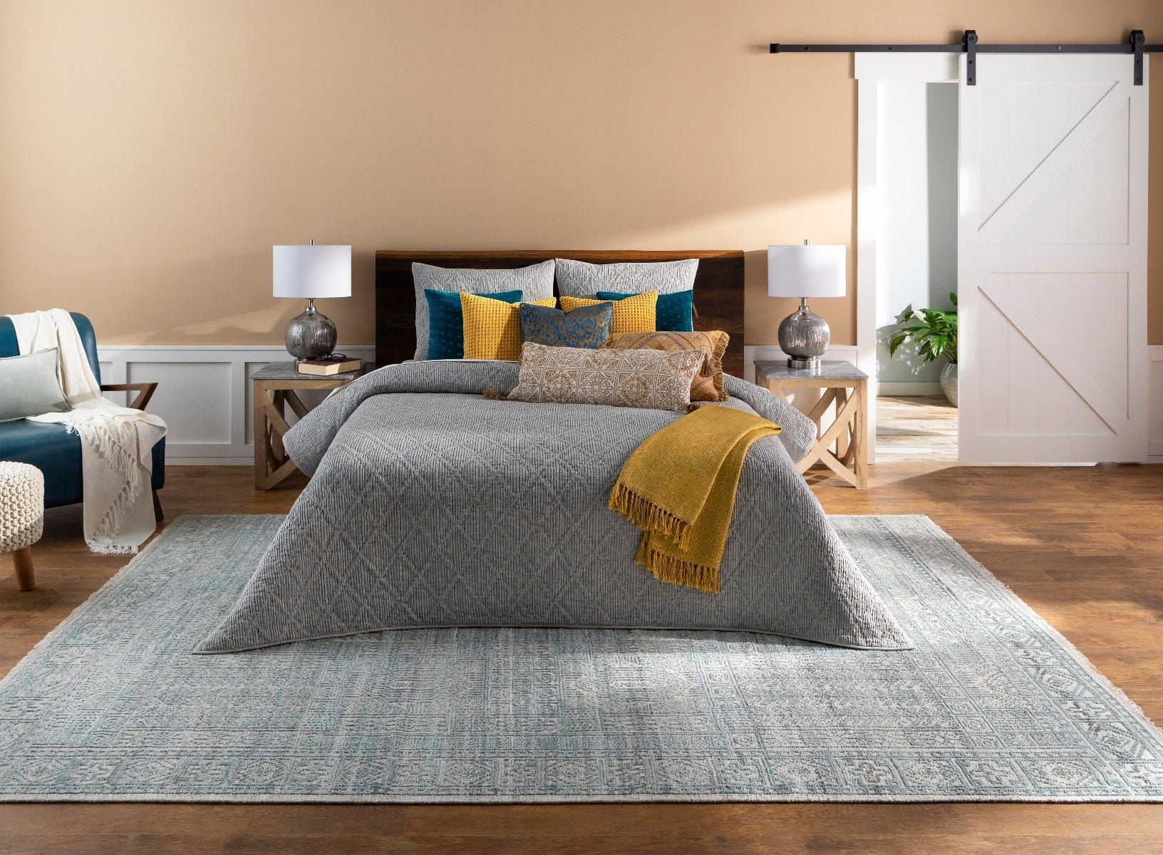 Bedroom with bed, rug, sliding door, and accent furniture in neutral tones with pops of blue and yellow.