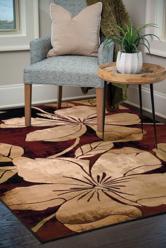 Floral-patterned rug with a beige and maroon design, chair, and a side table with a plant.