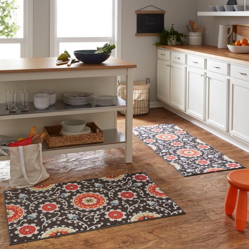 Two patterned rugs on a wood kitchen floor, near an orange stool and white cabinets.