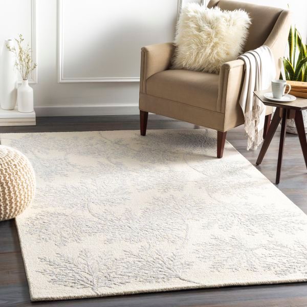 Cream-colored rug with subtle blue leaf design under a beige armchair with a fluffy pillow in a living room.